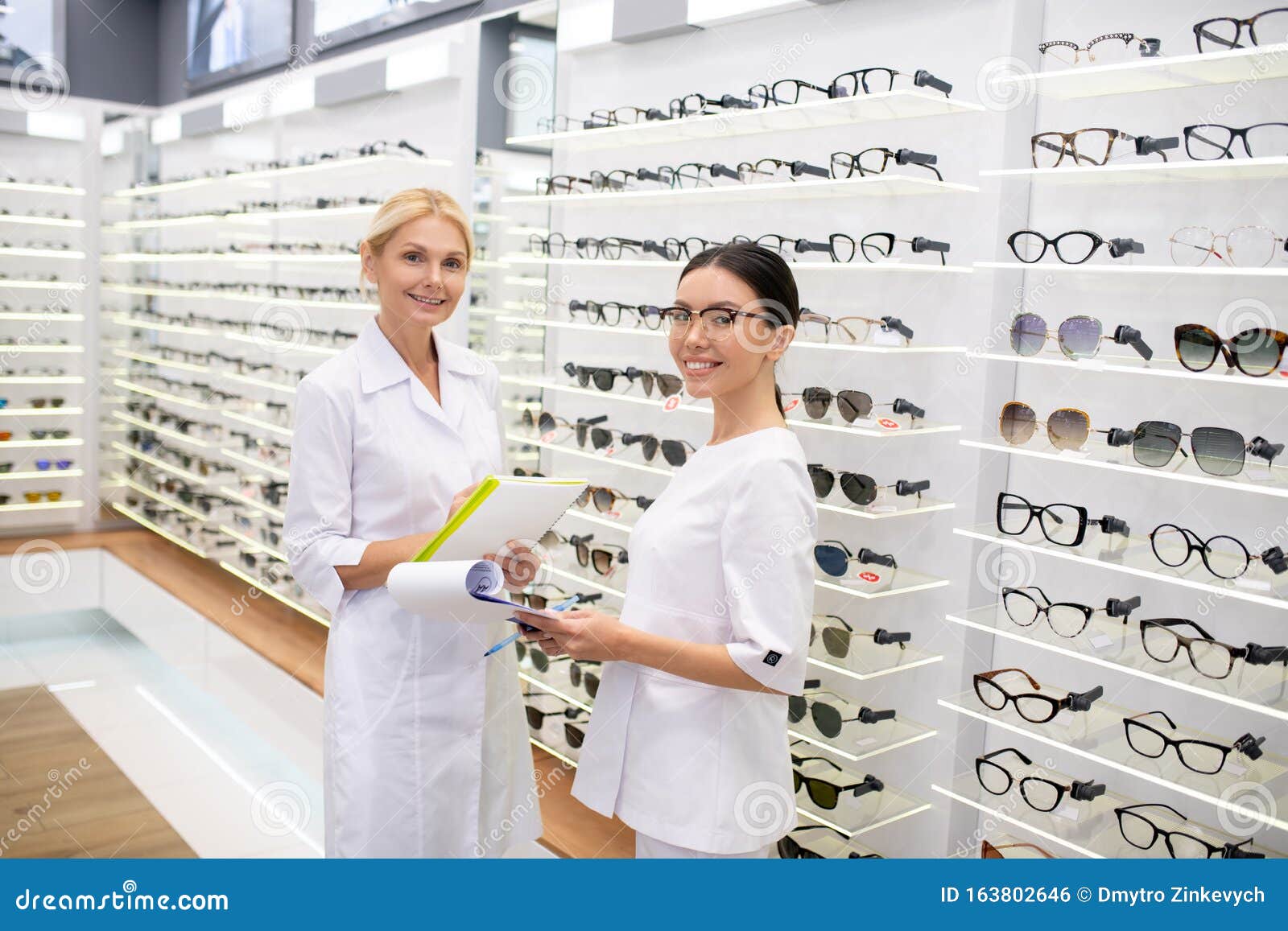 Cheerful Workers Of Optical Store Standing Near Shelves ...