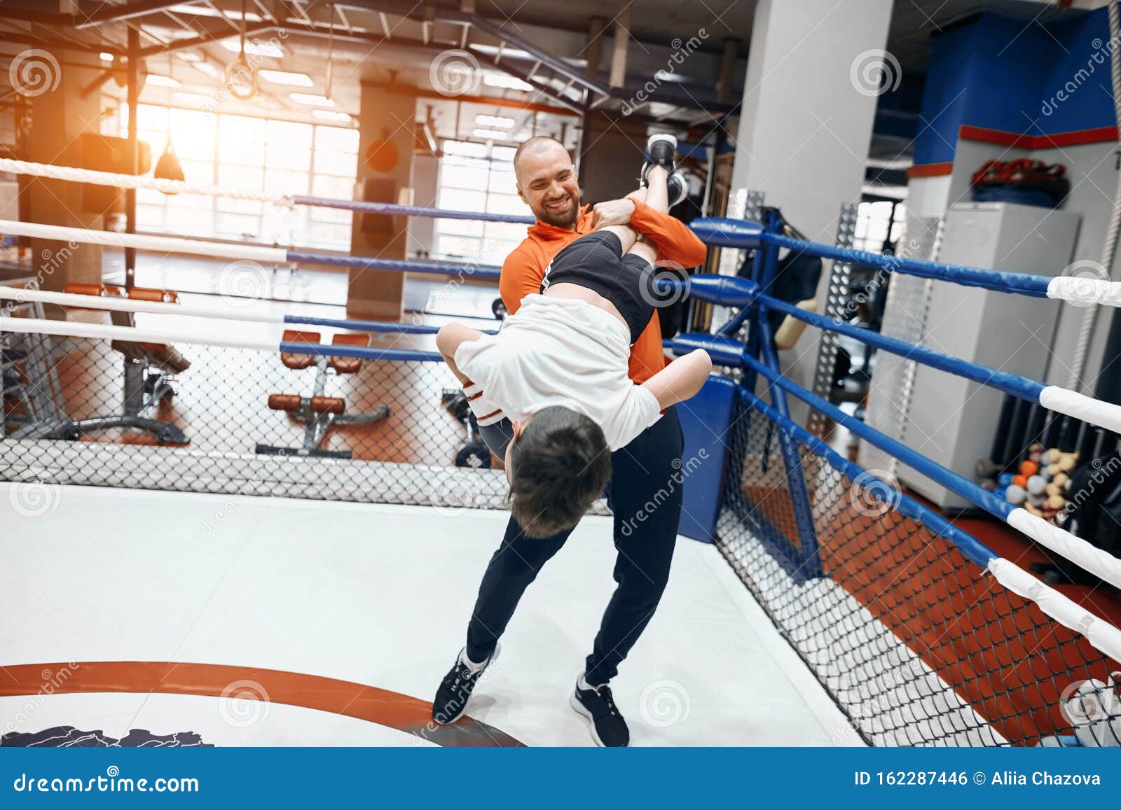 cheerful young coach and his student having great time at gym