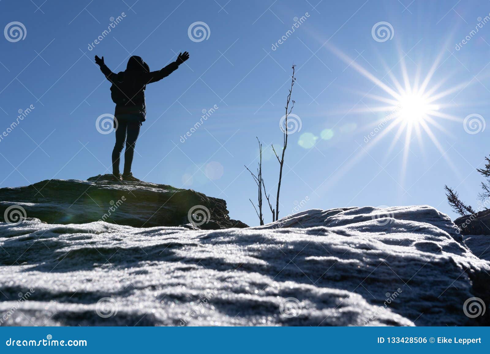 cheering woman hiker open arms at mountain peak backlit with heavy lensflare and ice crystalls in the foreground.