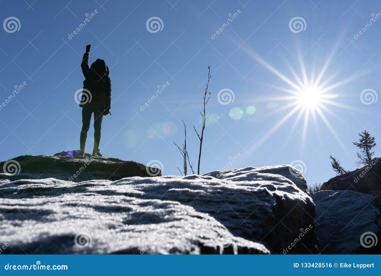 cheering woman hiker open arms at mountain peak backlit with heavy lensflare and ice crystalls in the foreground.