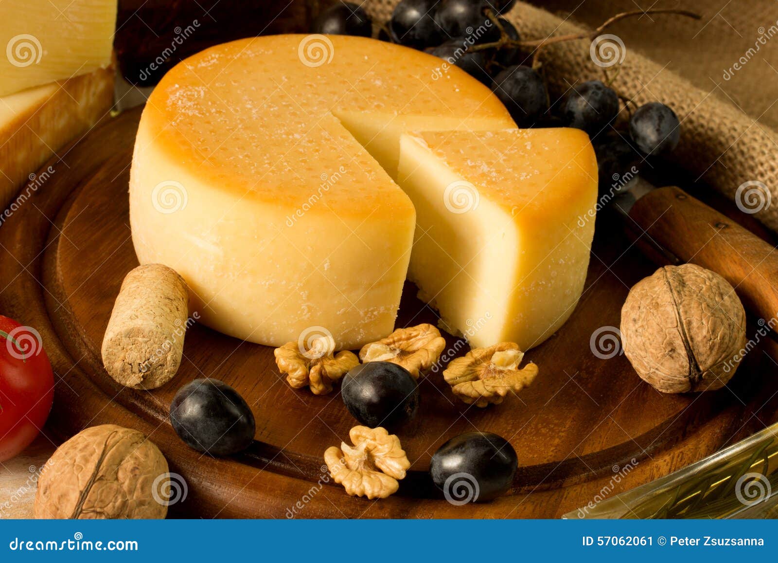 Round cheese on a cutting board, with nut and grape