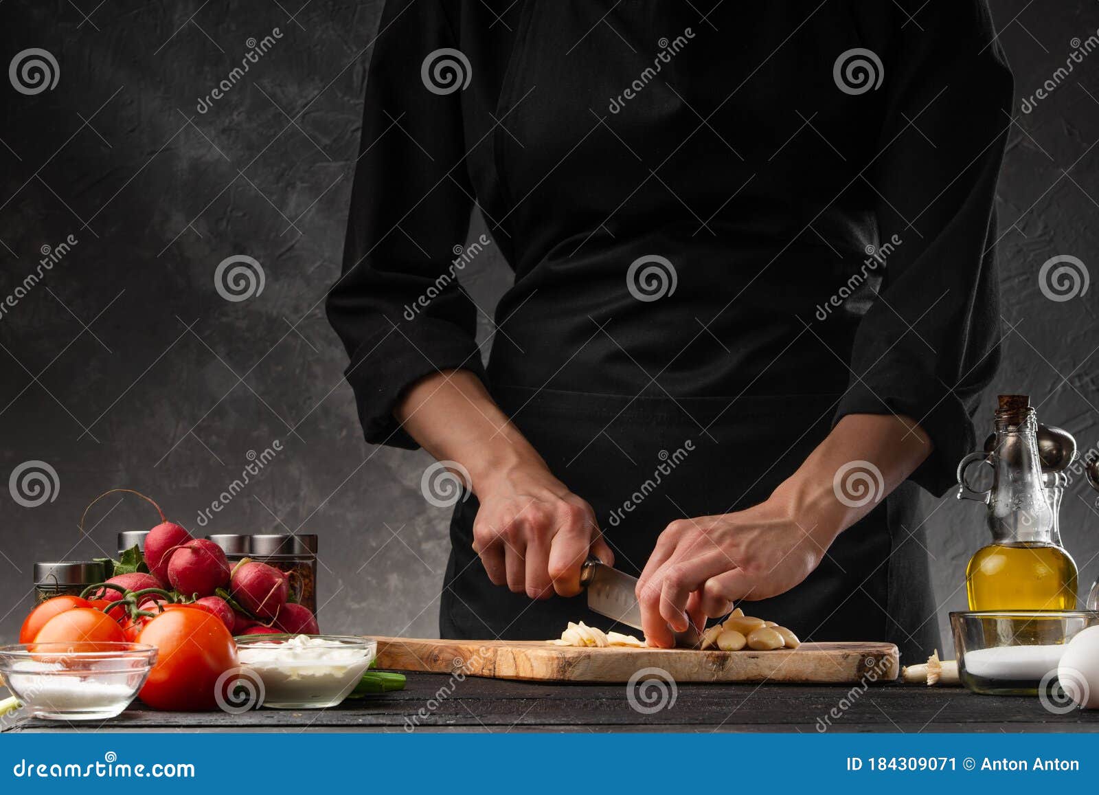 chef chopping garlic for cooking. against the background of a gray wall, and vegetables. cooking and recipe book