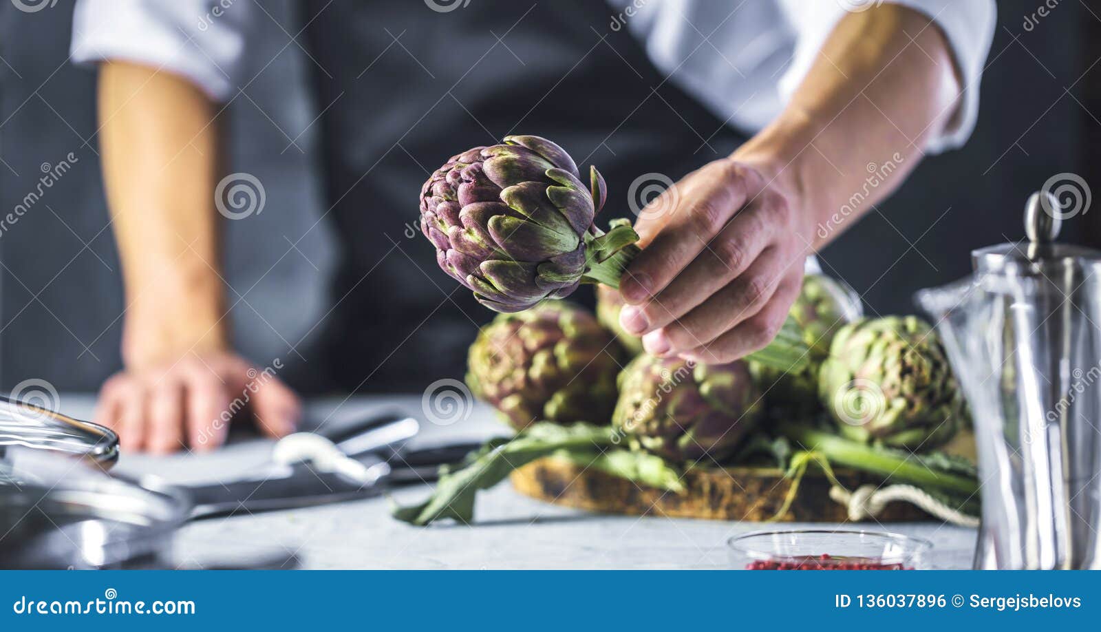 chef cutting artichokes for dinner preparation - man cooking inside restaurant kitchen