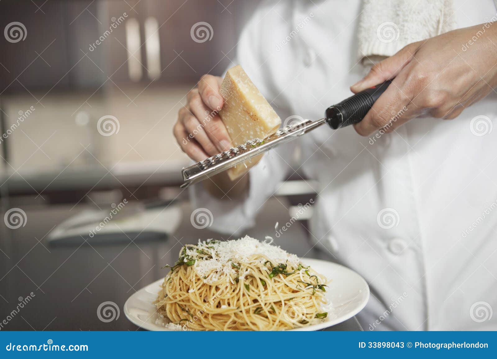 chef grating cheese onto pasta in kitchen