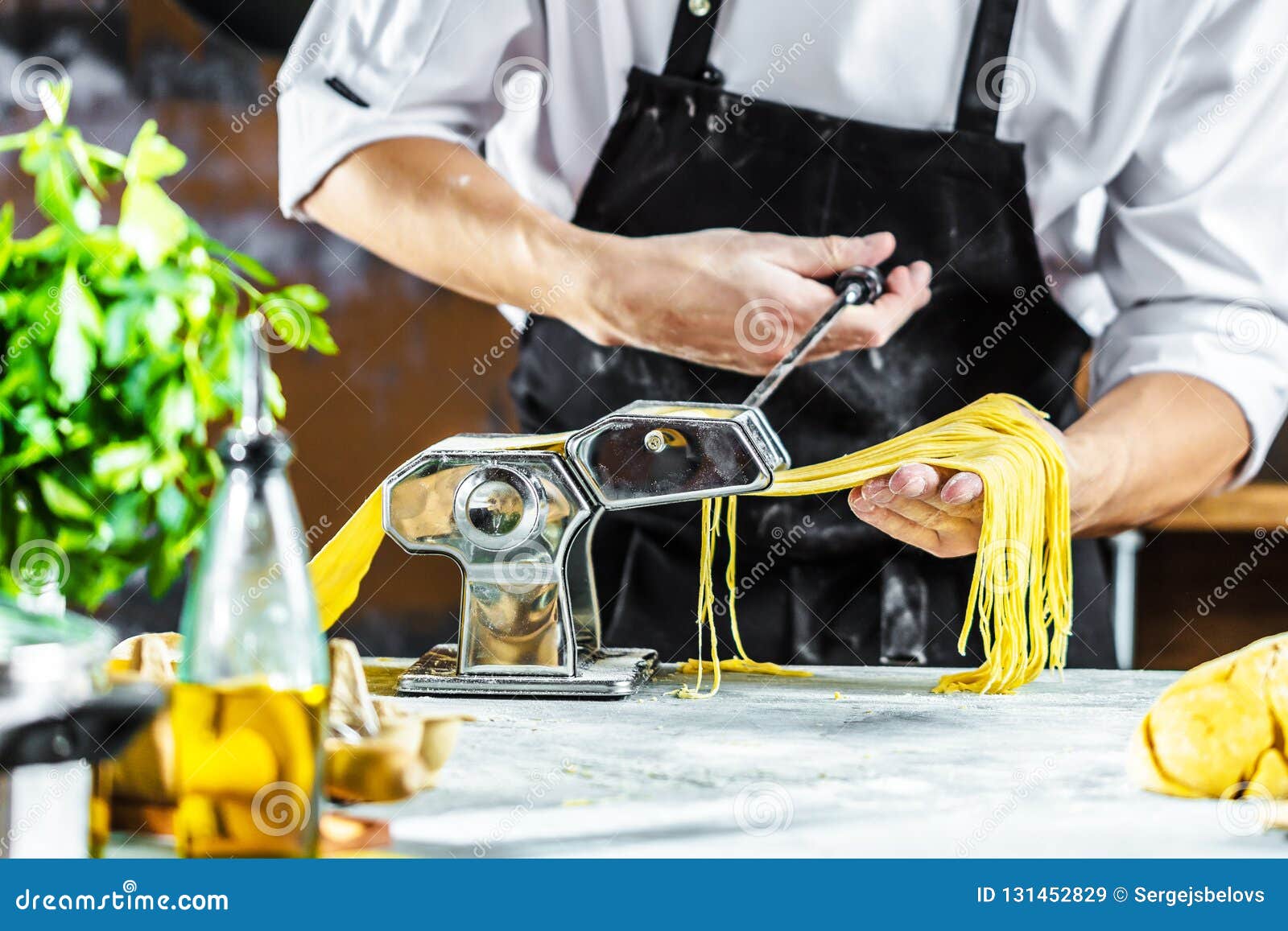 Chef Making Spaghetti Noodles with Pasta Machine on Kitchen Table with Some Ingredients Around