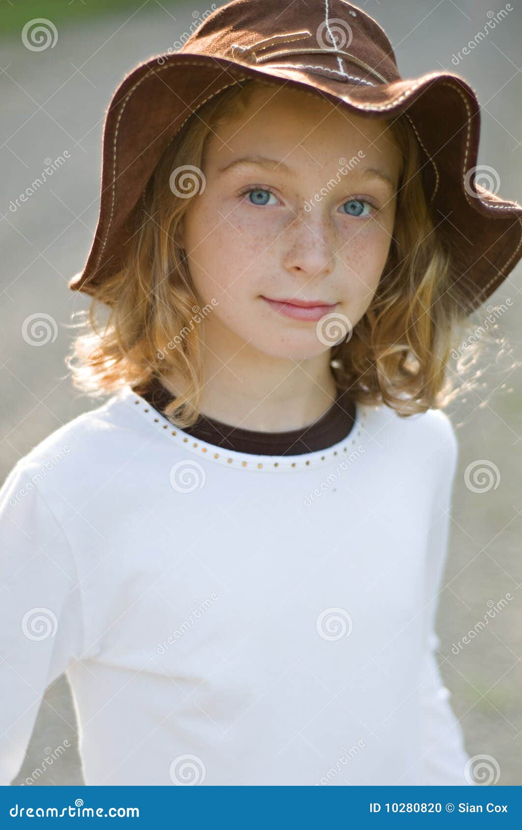 Chica joven en un sombrero del sol. Retrato de una chica joven que desgasta un sombrero marrón flojo grande del sol al aire libre por la tarde