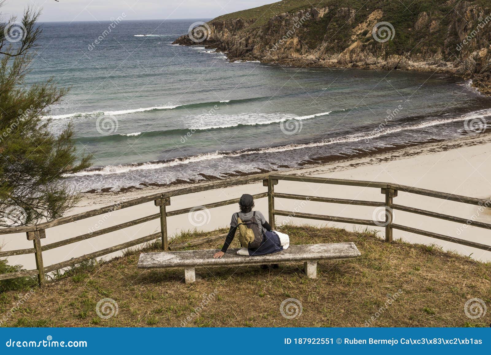 chica senderista descansa en un banco y disfruta de la vista panoramica de la playa de esteiro en la ruta de los faros