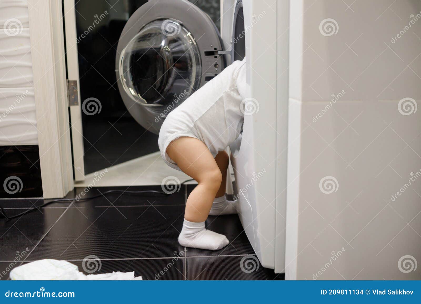 Child Climbing into Frontloading Washing Machine. Side View Stock