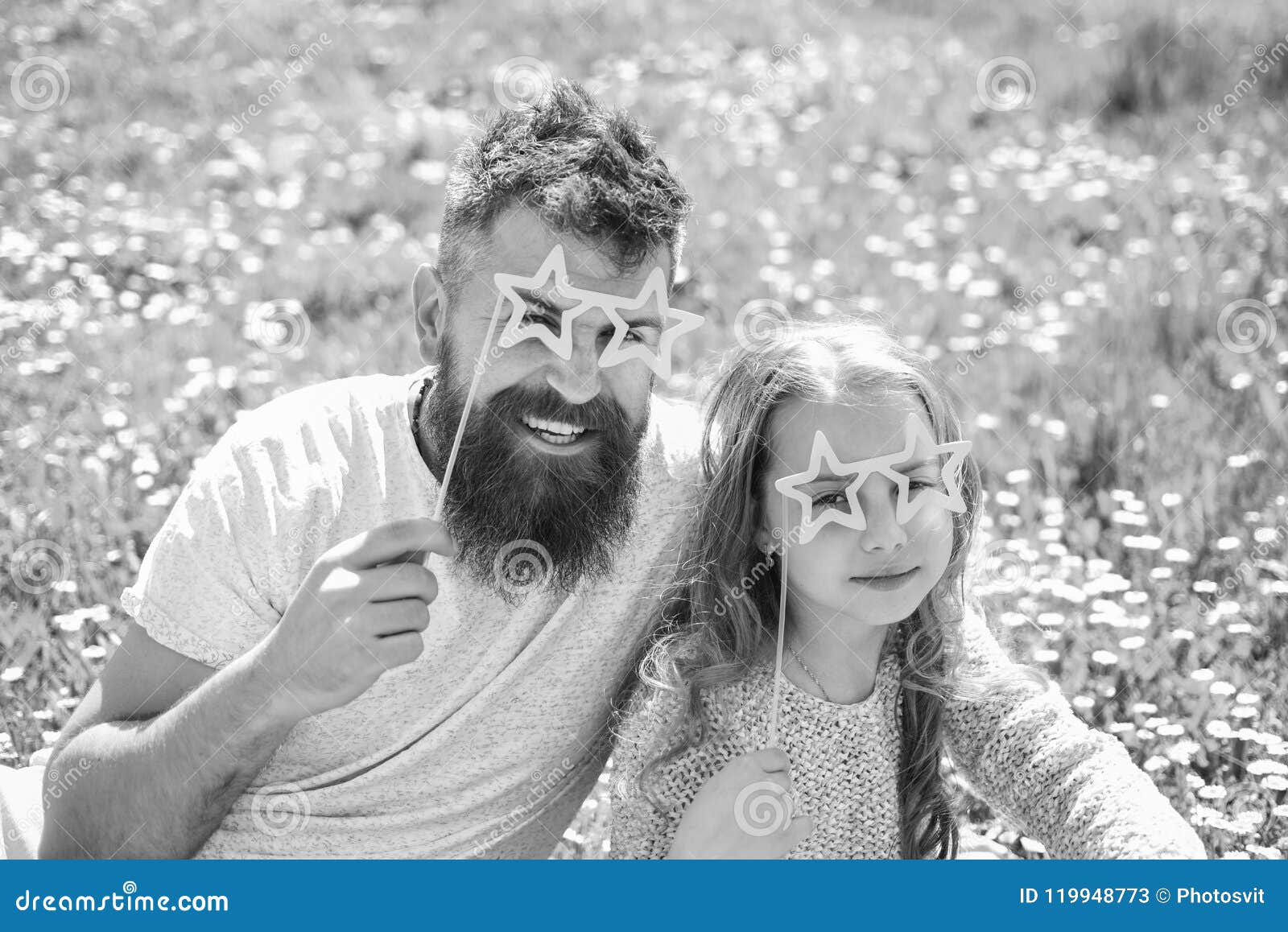 child and dad posing with star d eyeglases photo booth attribute at meadow. father and daughter sits on grass at