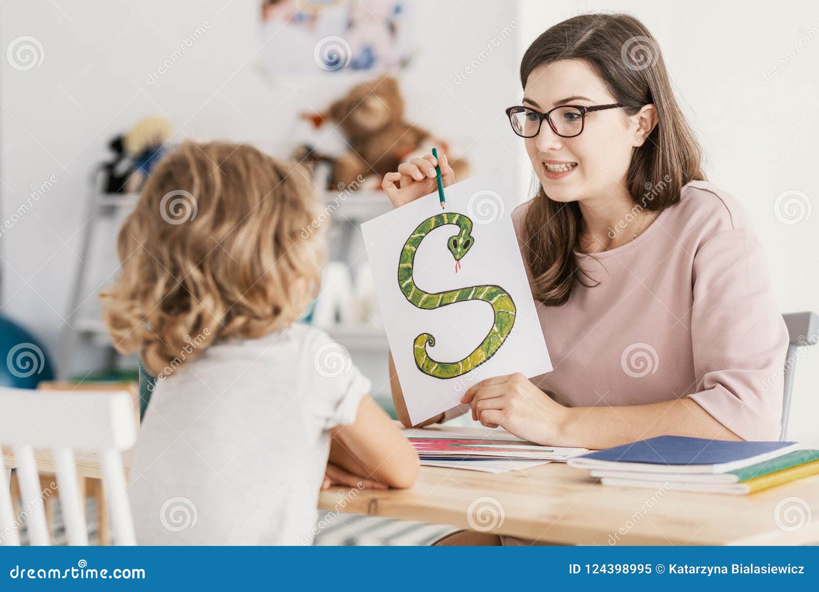 a child with development problems with a professional speech therapist during a meeting. tutor holding a prop poster of a snake as