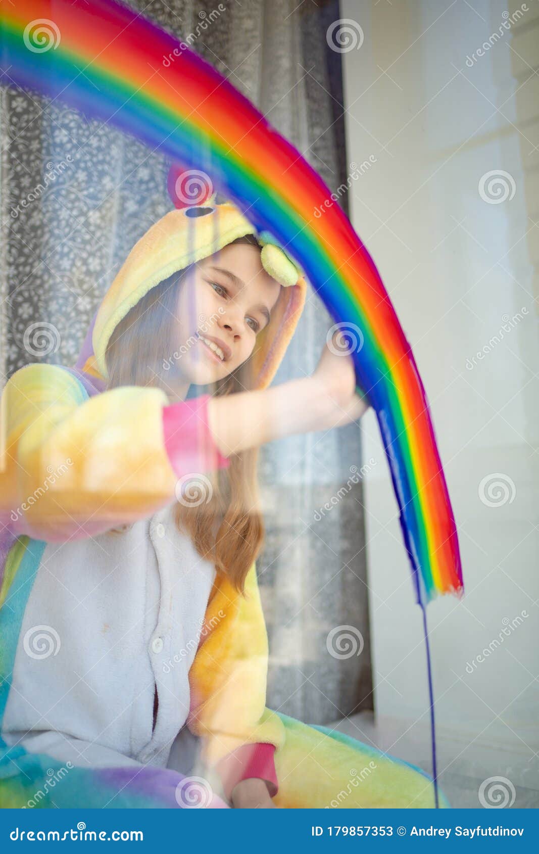 child girl in kigurumi draws rainbow on window.