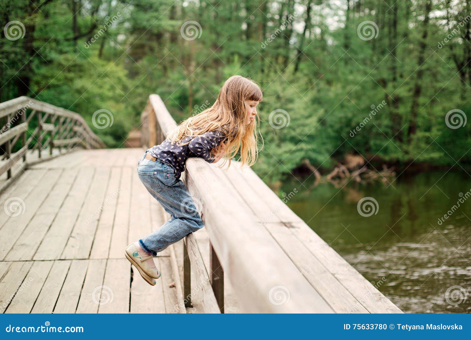 child girl sitting on a wooden bridge near the water on the rive
