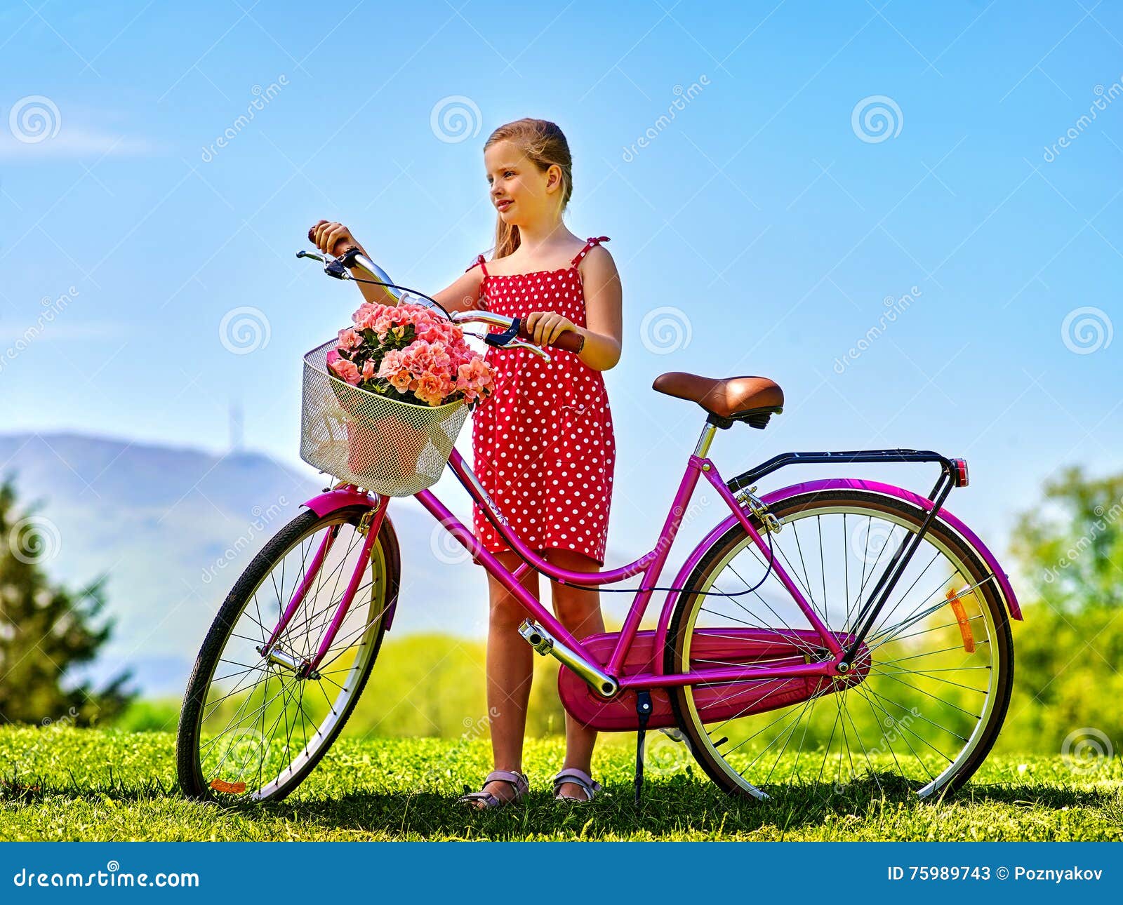 child girl wearing sundress rides bicycle into park.
