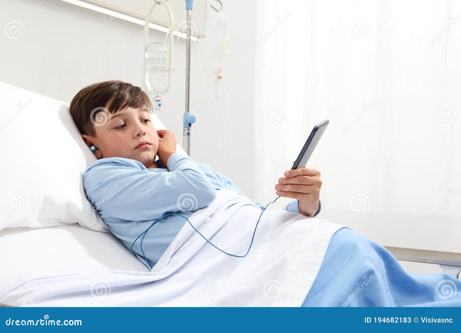 child in hospital bed using smartphone surfs the internet wearing earphones