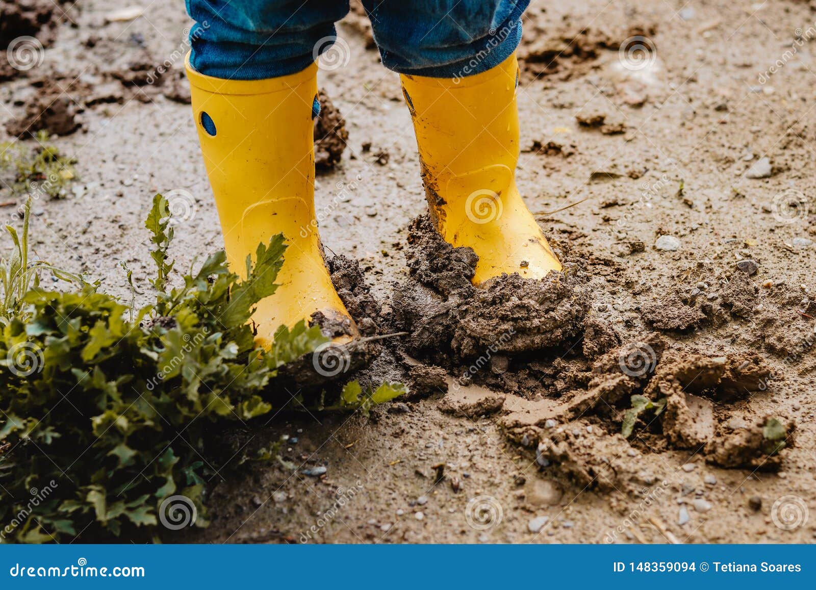 child legs in yellow muddy rubber boots on wet mud.  baby playing with dirt at rainy weather.