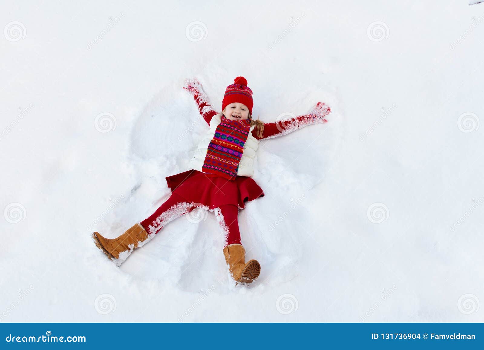 child making snow angel on sunny winter morning. kids winter outdoor fun. family christmas vacation. little girl playing in snow