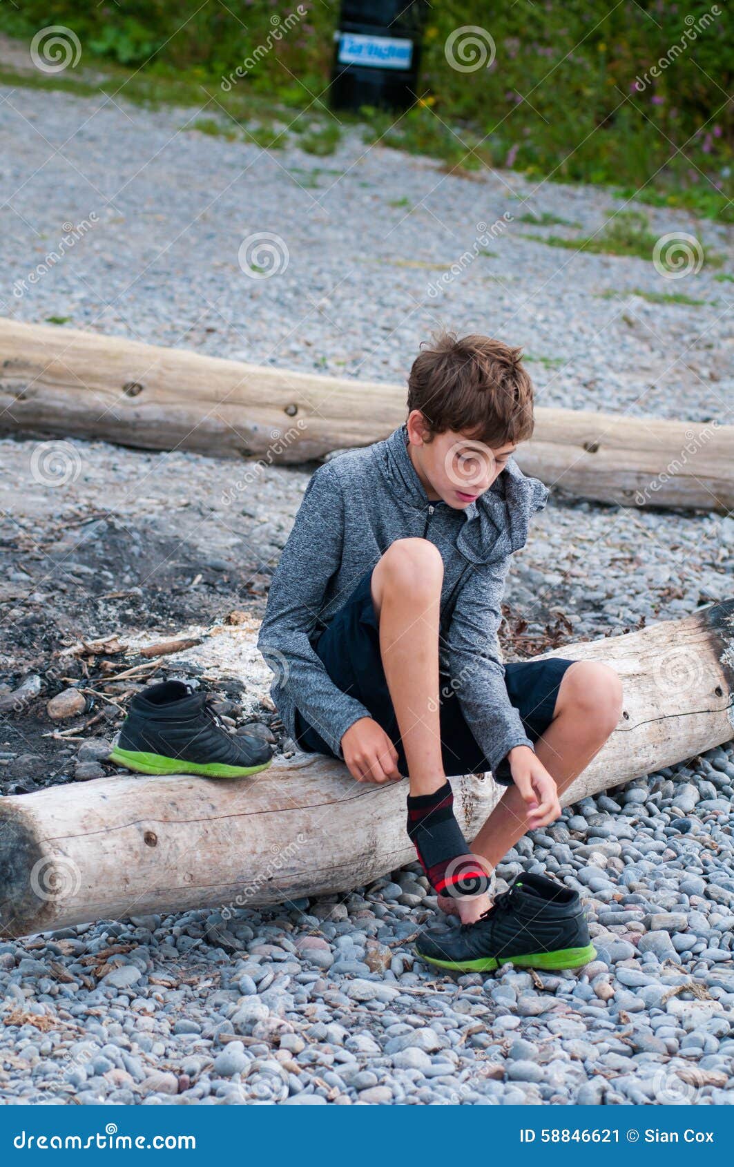 Young Boy Sitting On A Bench Putting On His Shoes At The 