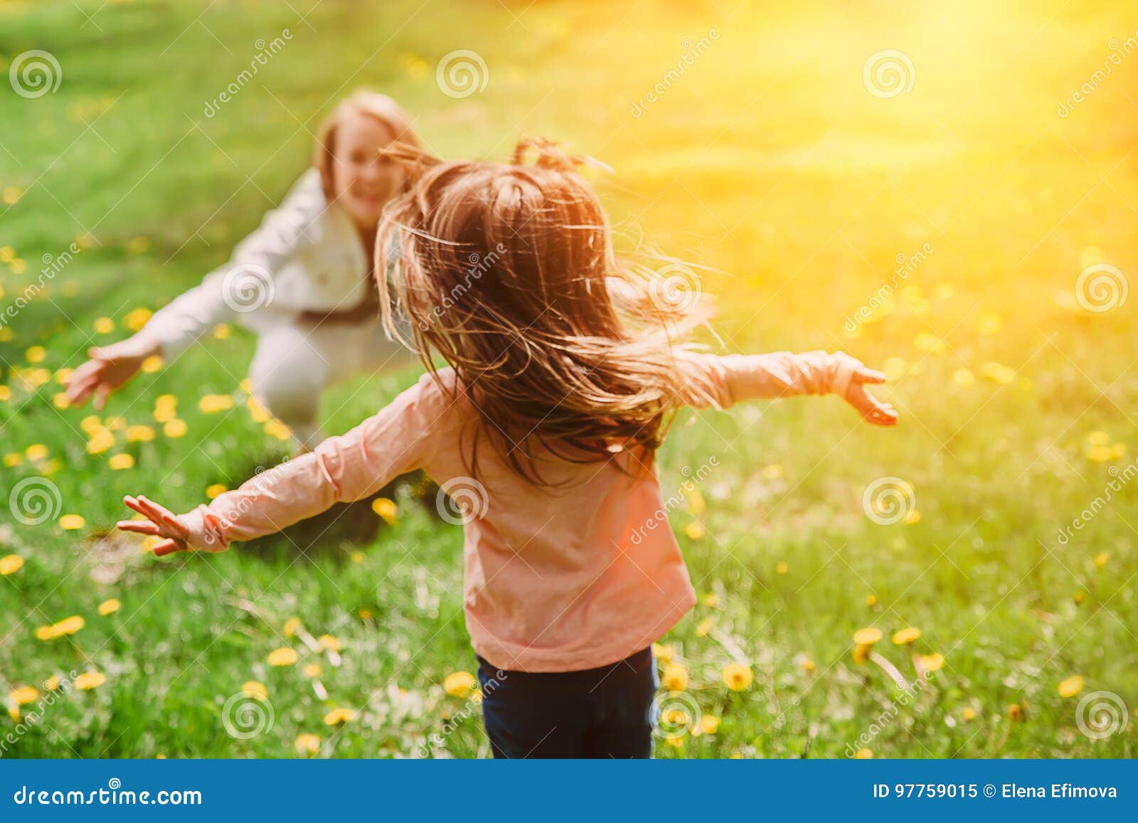 child running into mother`s hands to hug her. family having fun in the park.