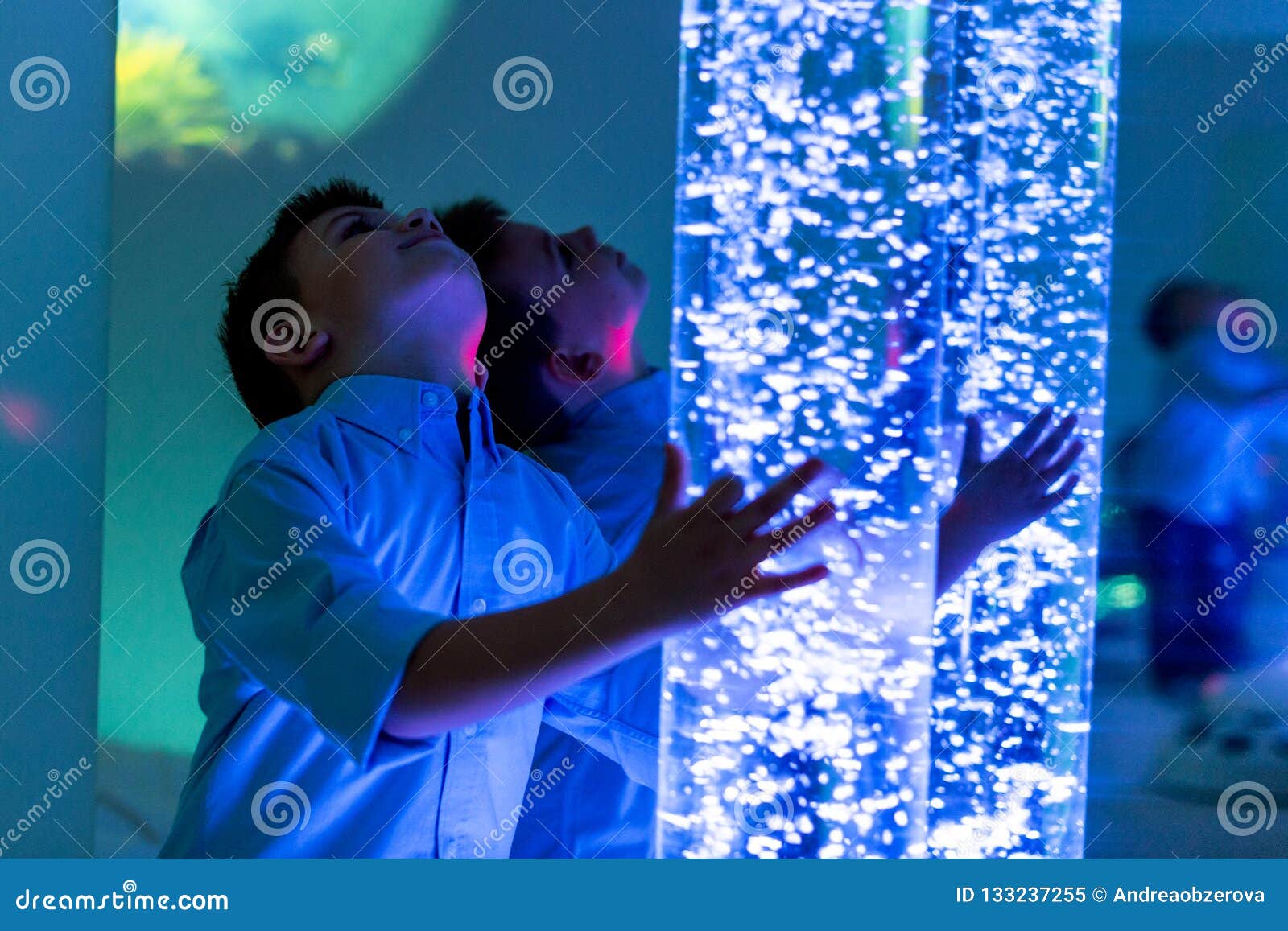 child in therapy sensory stimulating room, snoezelen. child interacting with colored lights bubble tube lamp during therapy.