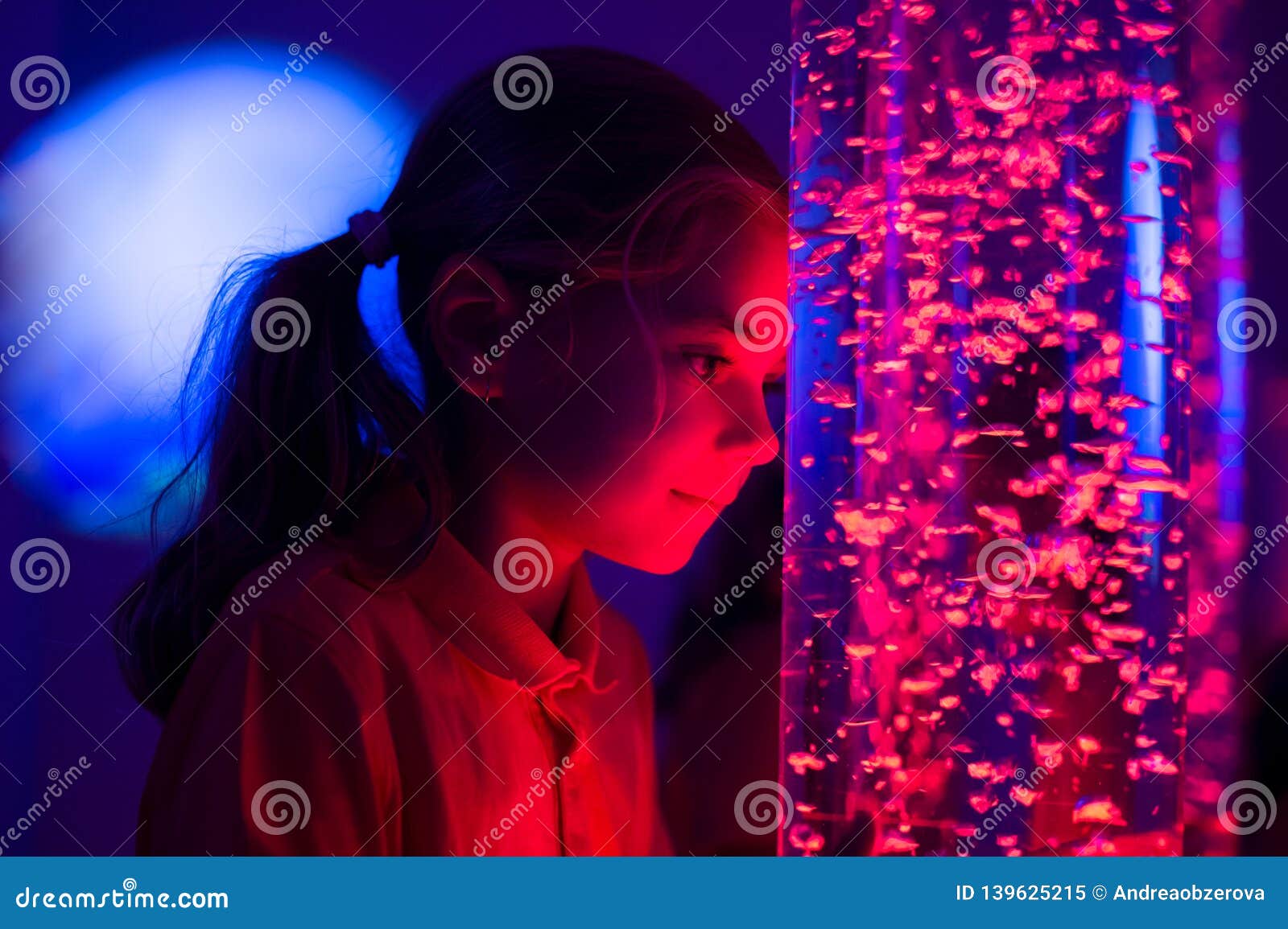 child in therapy sensory stimulating room, snoezelen. child interacting with colored lights bubble tube lamp during therapy.