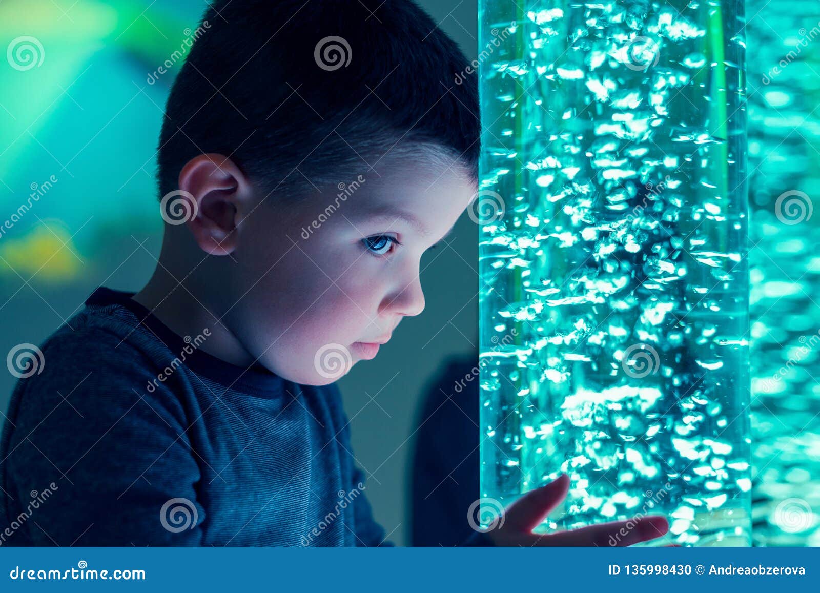 child in therapy sensory stimulating room, snoezelen. child interacting with colored lights bubble tube lamp during therapy.