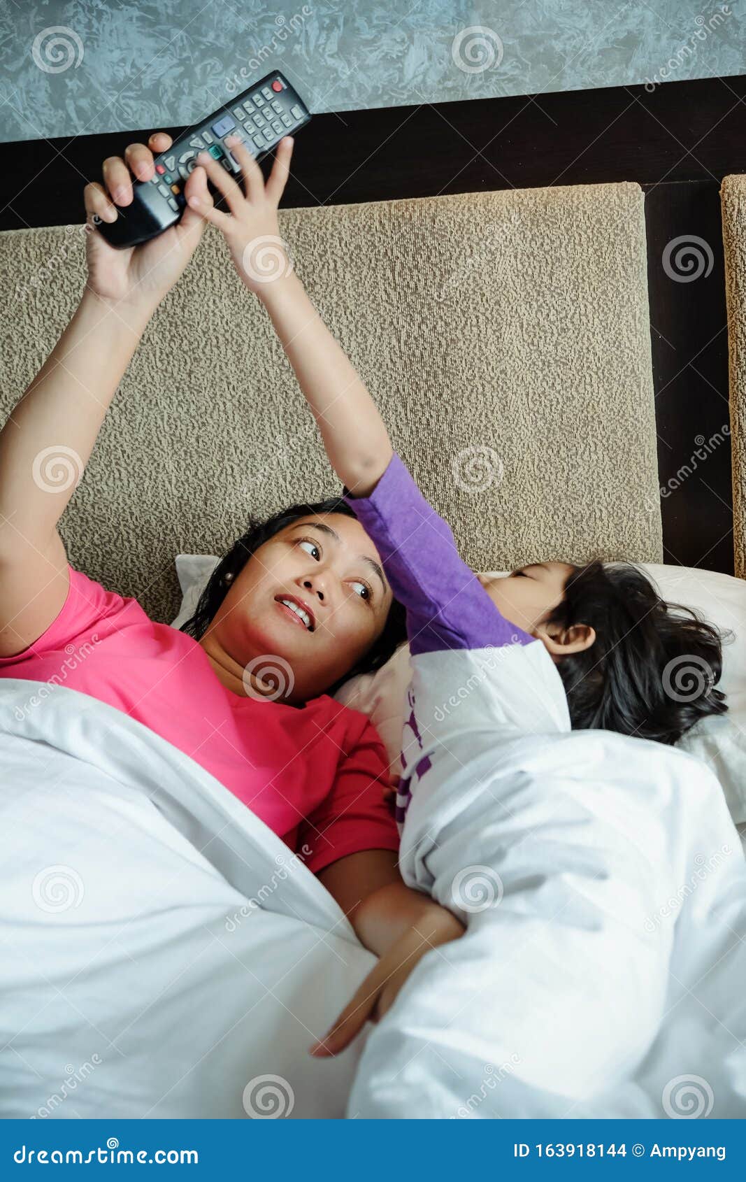 asian child on bed wants to take over television remote control from his mother. parental control