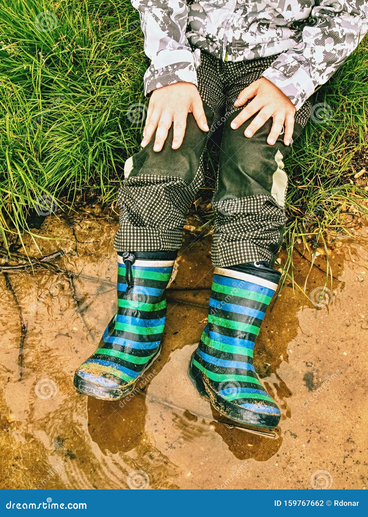 child wearing rain boots , sits at muddy puddle
