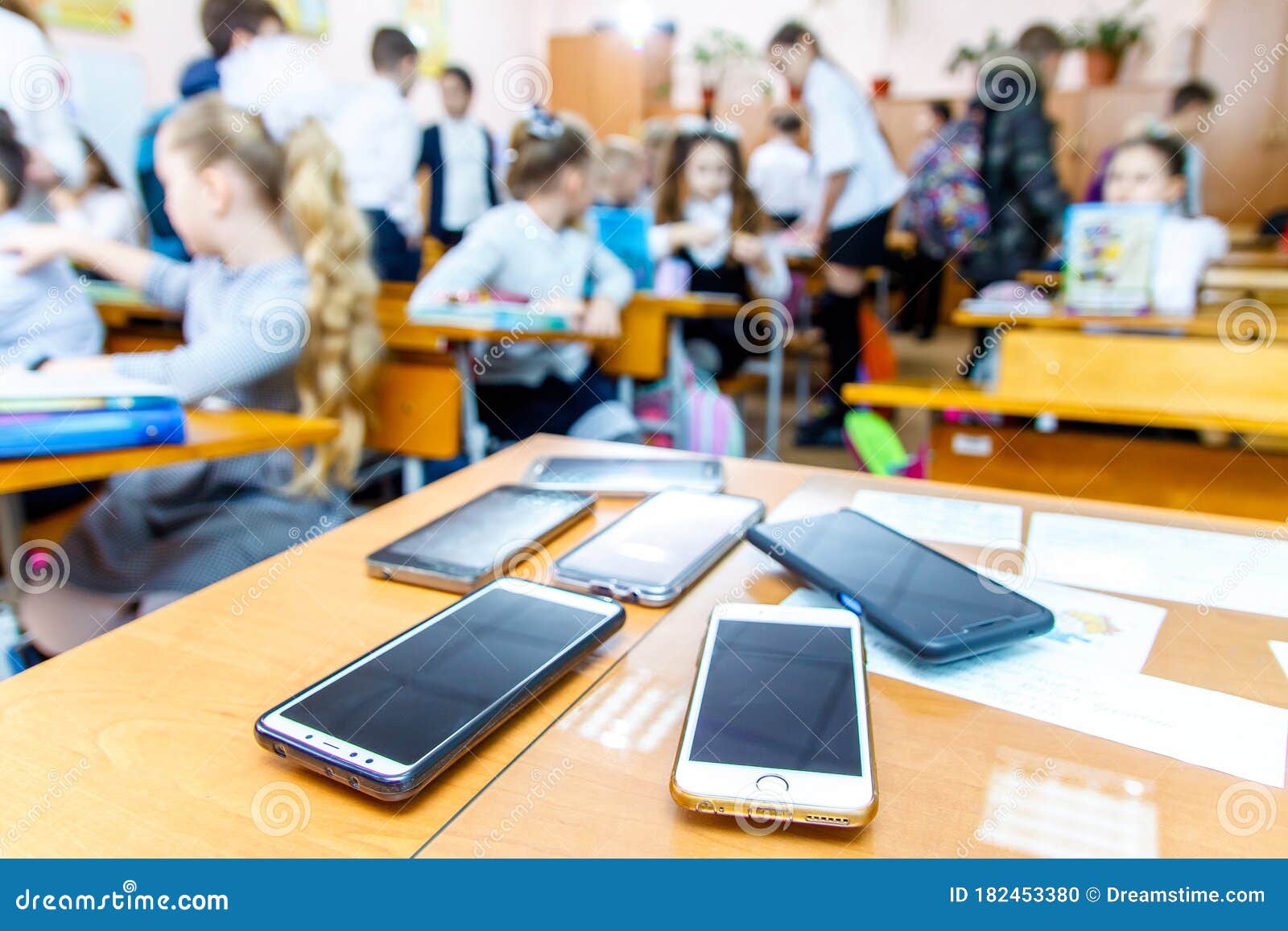 children mobile phones stand on a teacher`s desk in a school class