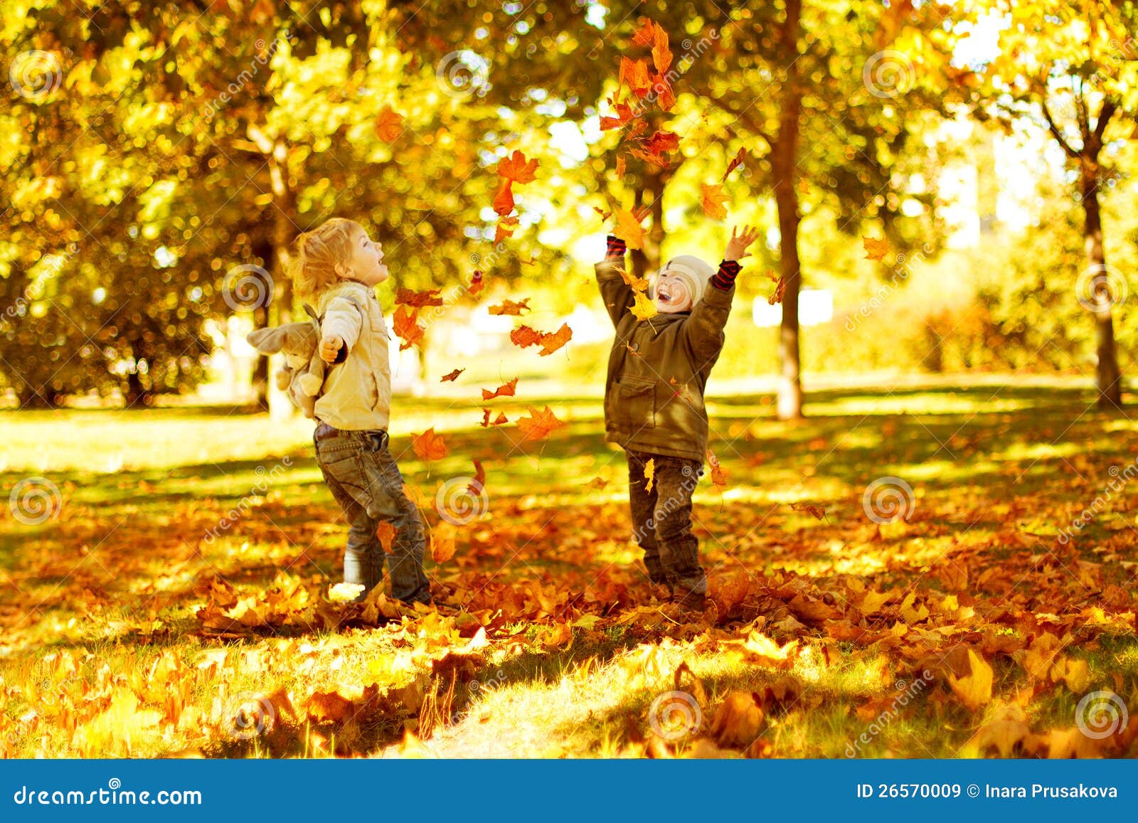 children playing with autumn fallen leaves in park