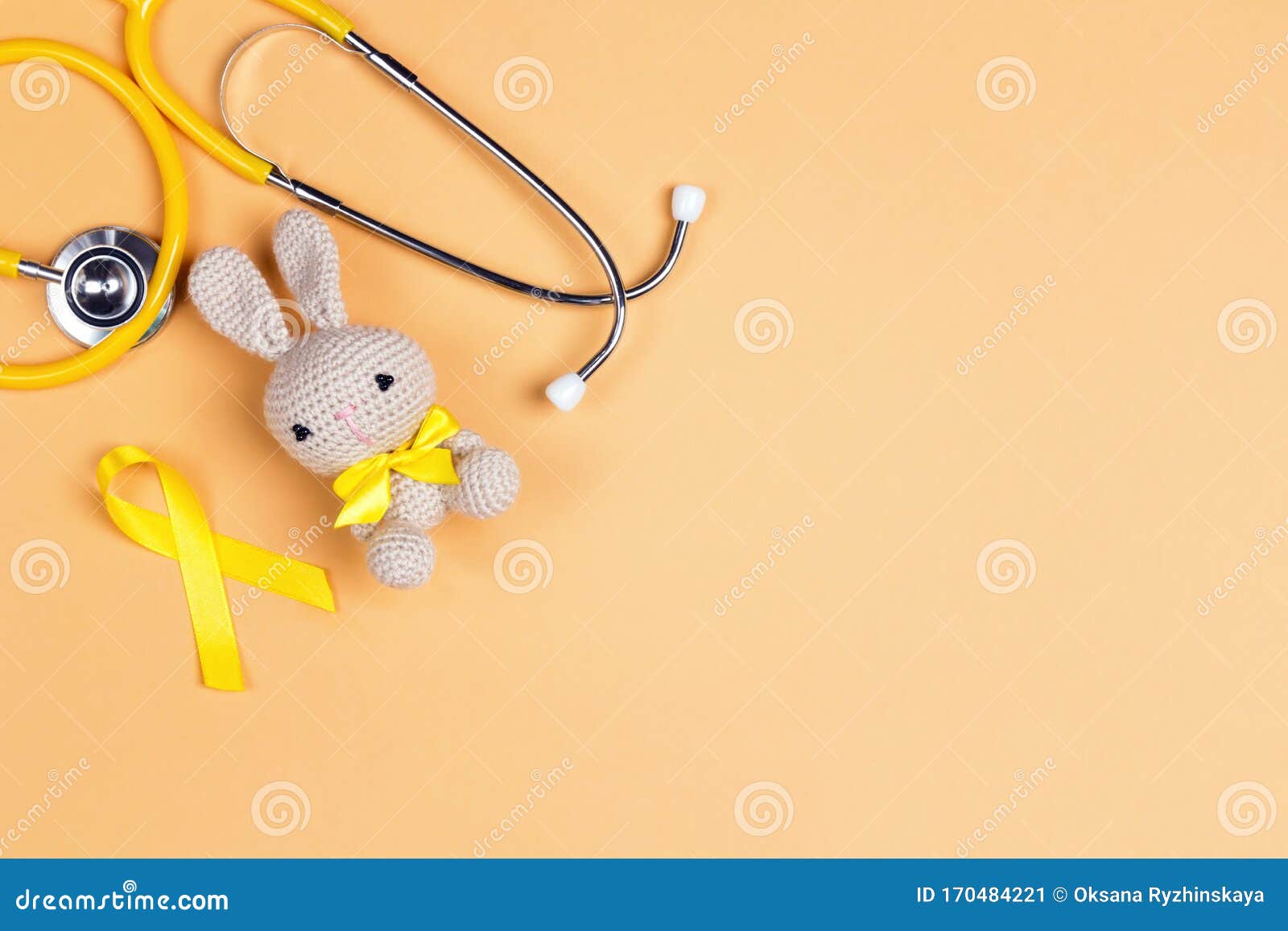 children`s toy with a childhood cancer awareness golden ribbon and stethoscope on yellow background with copy space