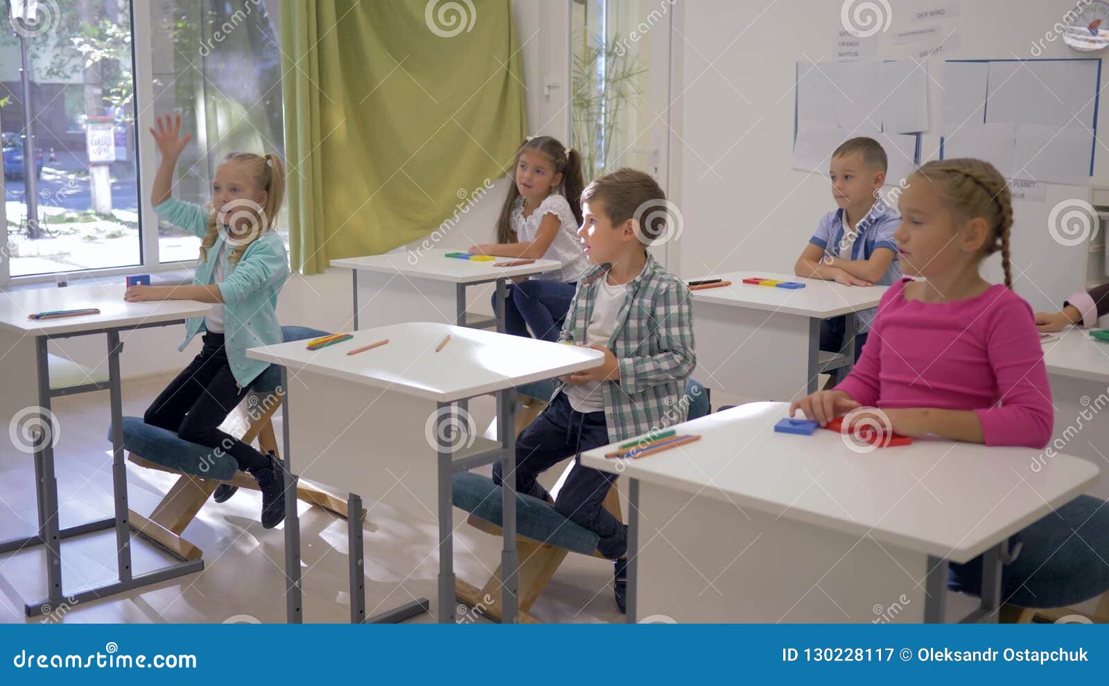 Children At School Boys And Girls Sit At Desks And Raise Hands