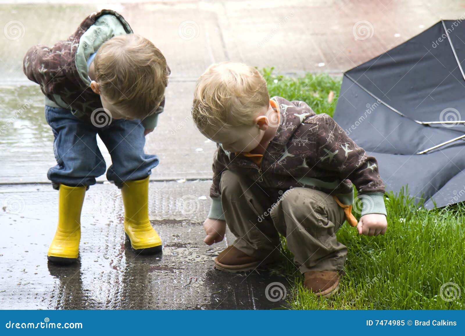 Two three year old children watch worm crawling on sidewalk