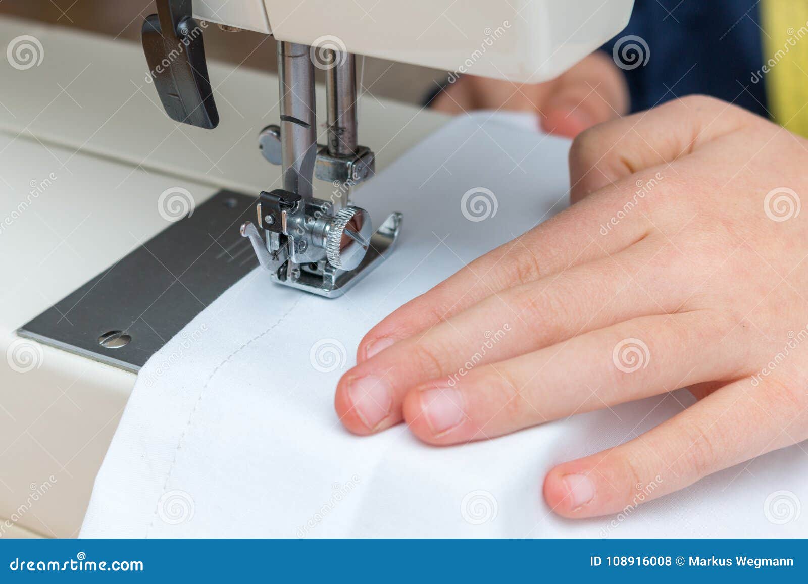 a childs hand pulling a white textil throught a sewing machine