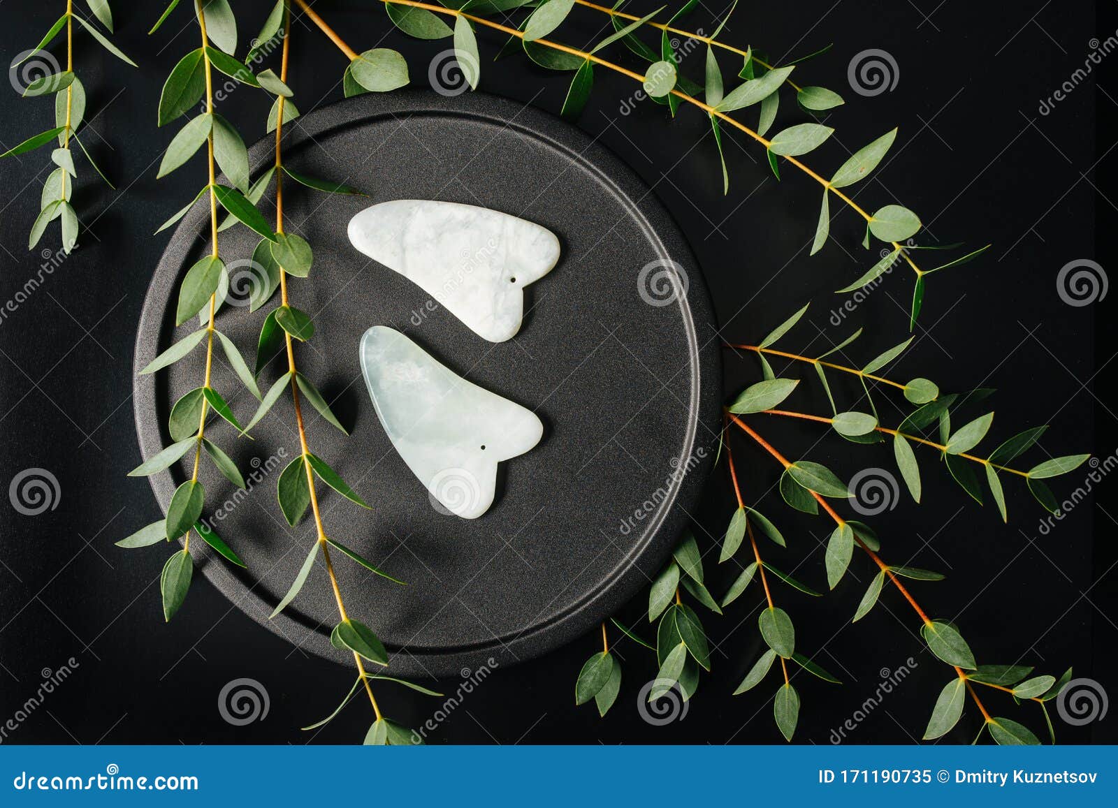 gua sha stones on a plate with eucalyptus branches over black. top view