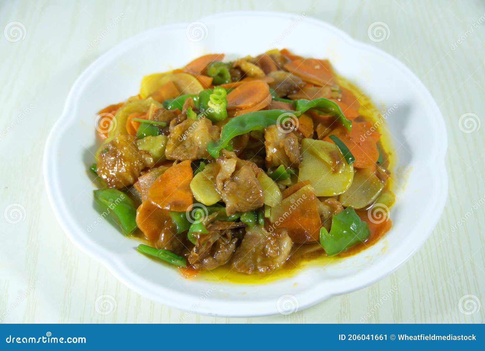 chinese stir-fried fresh meat with carrots, green peppers, potatoes on white plate, top view