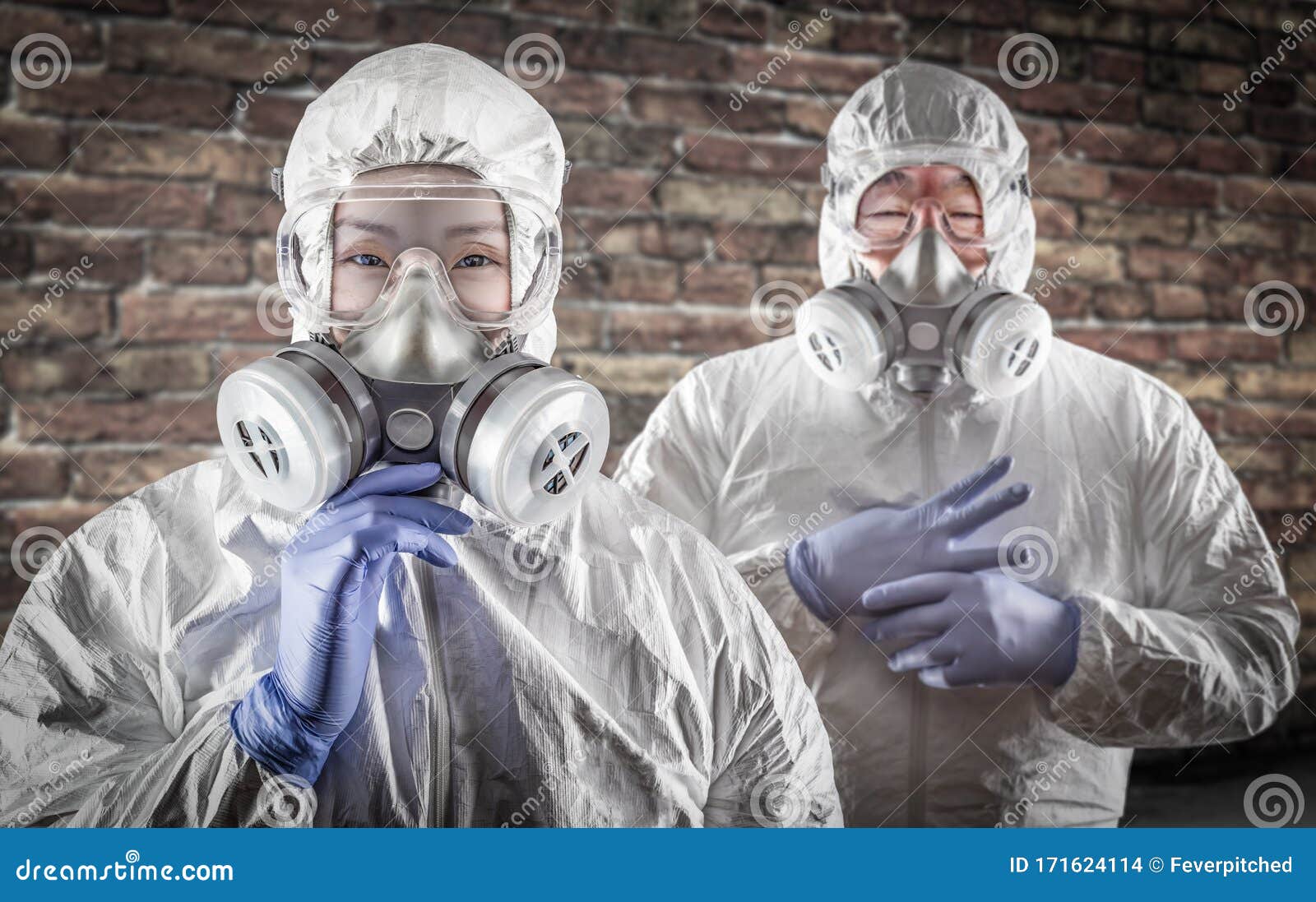 chinese woman and man in gas masks, goggles and hazmat suites against brick background