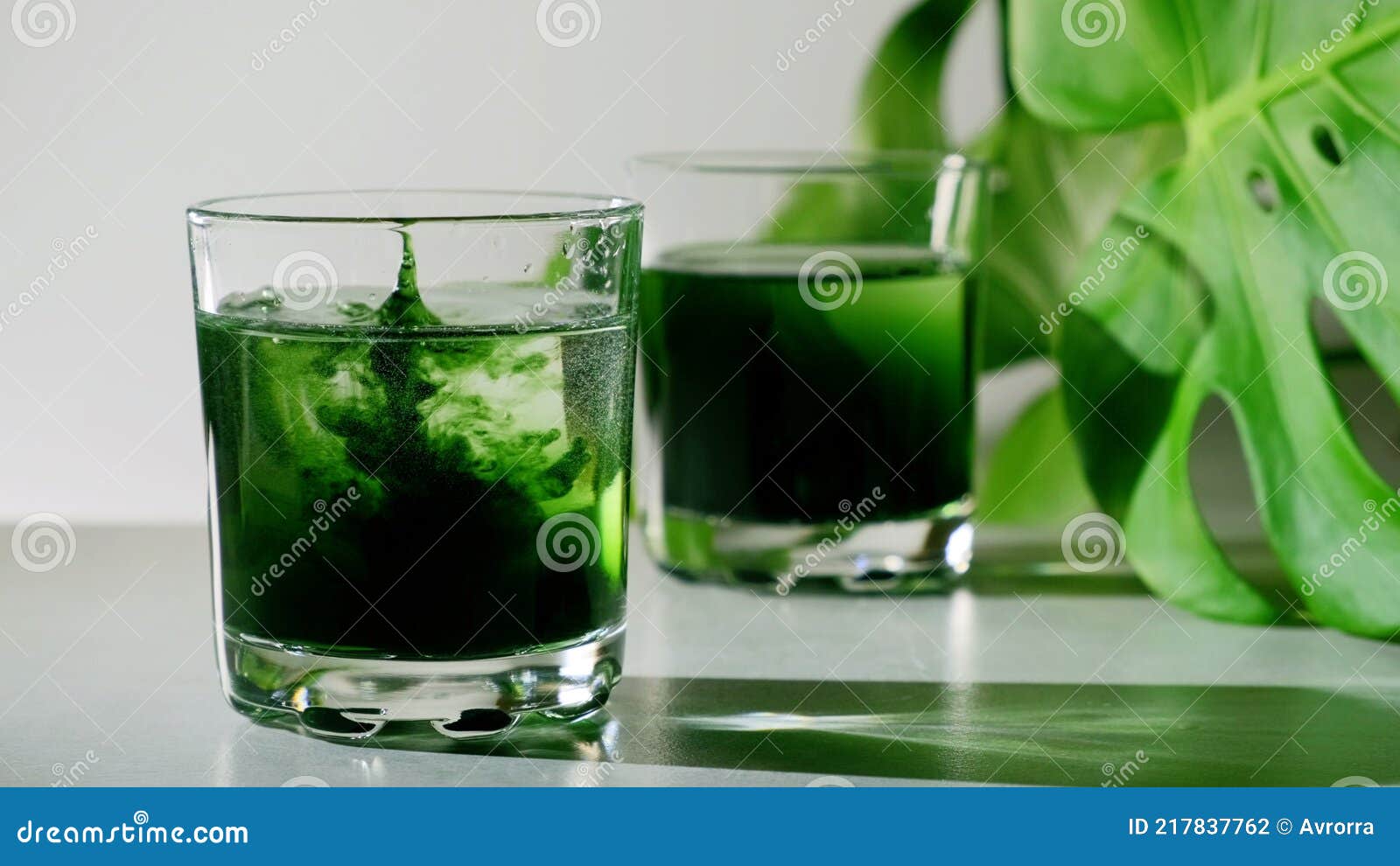 chlorophyll extract is poured in pure water in glass against a white grey background with green leaf