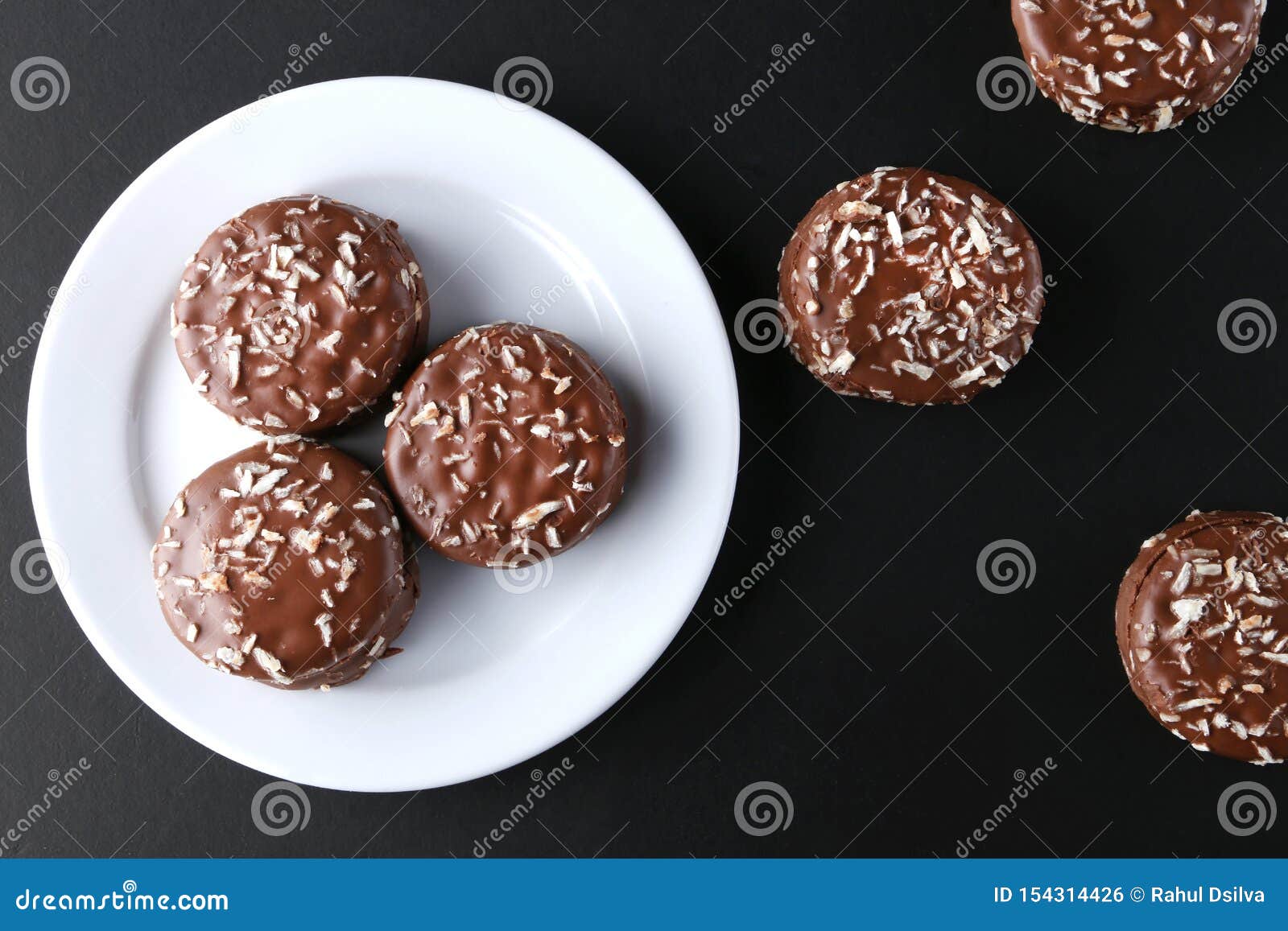 chocolate cookies with coconut shaving chocolate coating and coconut on wooden black  background.