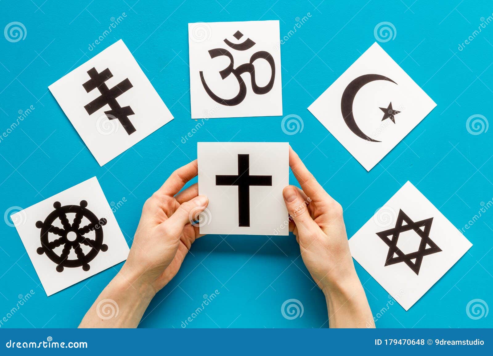 choose religion concept. hand with catholic cross near world religions s on blue background top view