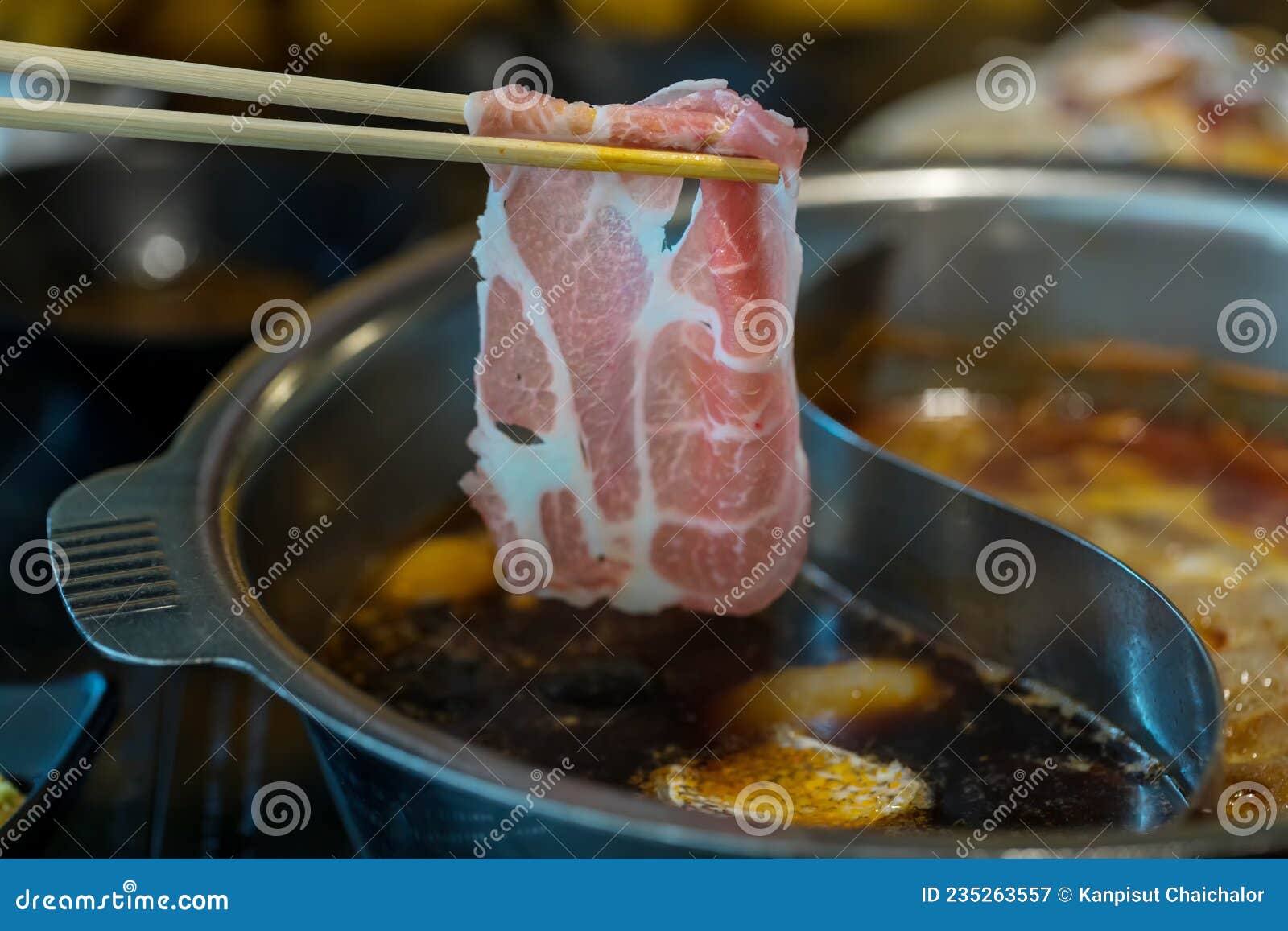 chopsticks take beef slice into shabu shabu pot,  healthy food. japanese cuisine, japanese beef shabu-shabu on wooden table. sukiy