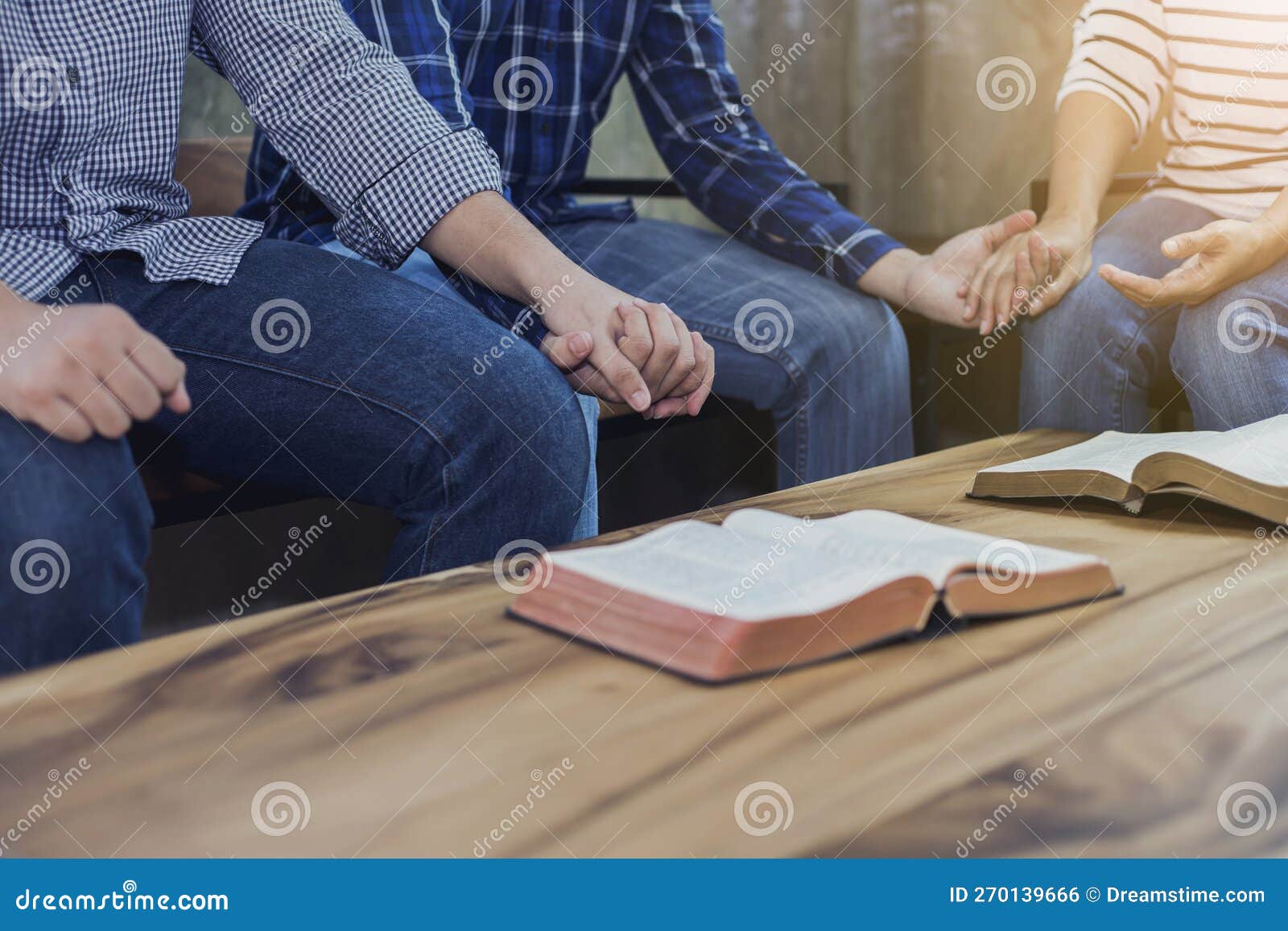 a christian group holding hands and together over blurred bible on wooden table, fellowship or bible study concept