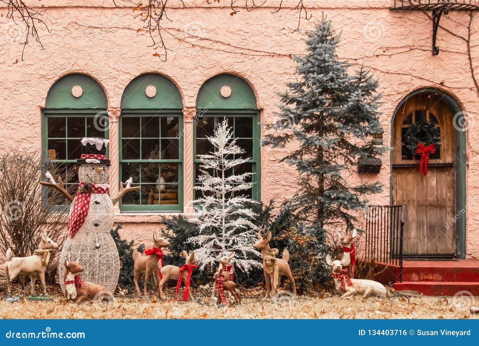 christmas forest tableau with snowman and be-ribboned deer outside windows of pink stucco house