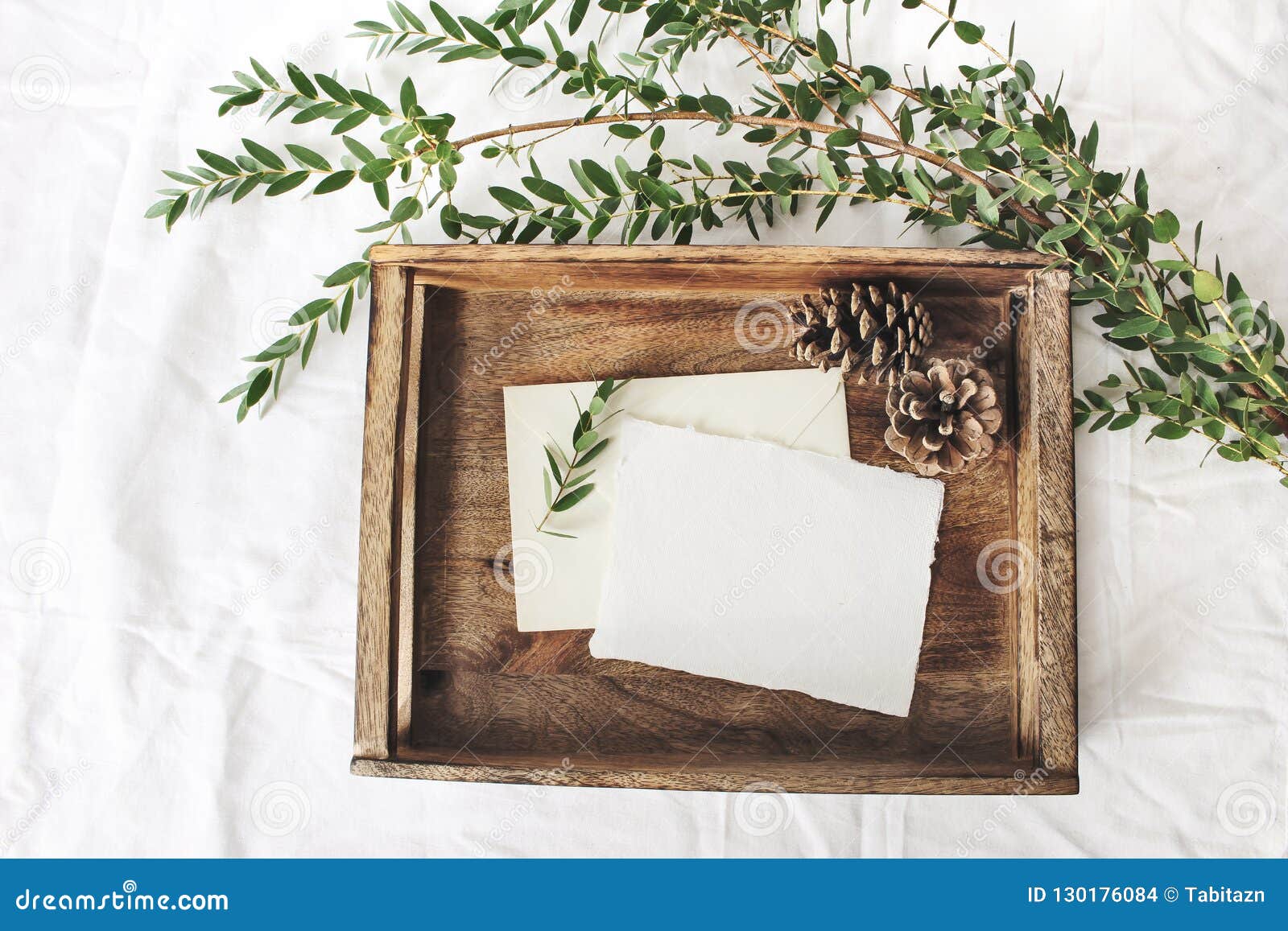 christmas or winter wedding mock-up scene. blank cotton paper greeting cards, old wooden tray, pine cones and green