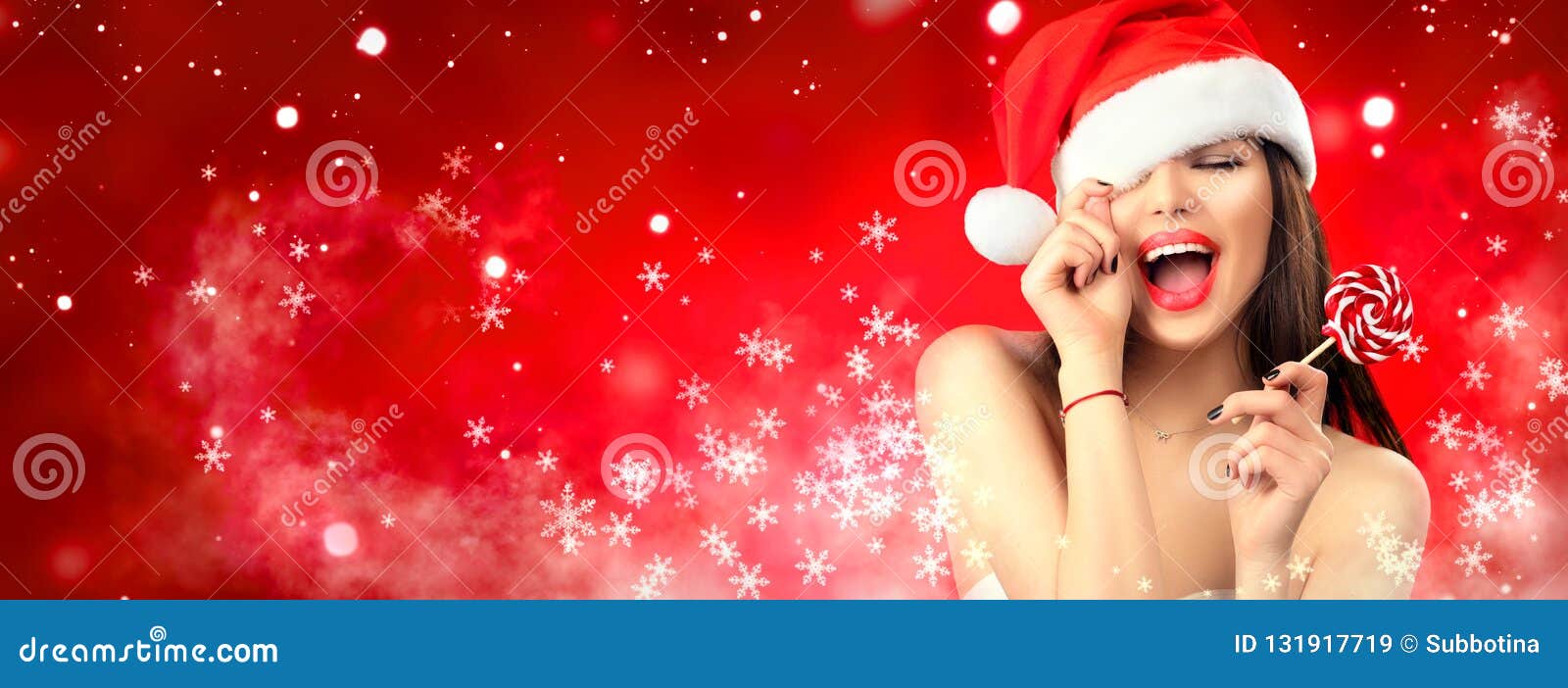 christmas woman. joyful model girl in santa`s hat with red lips and lollipop candy in her hand