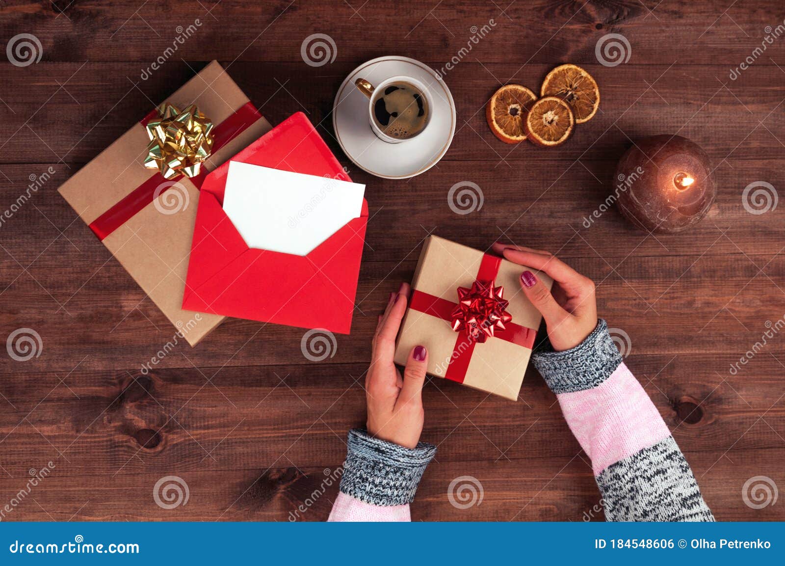 christmas workplace top view. girlÃ¢â¬â¢s hands on the wooden table holding christmas preset. christmas wreath, decorations