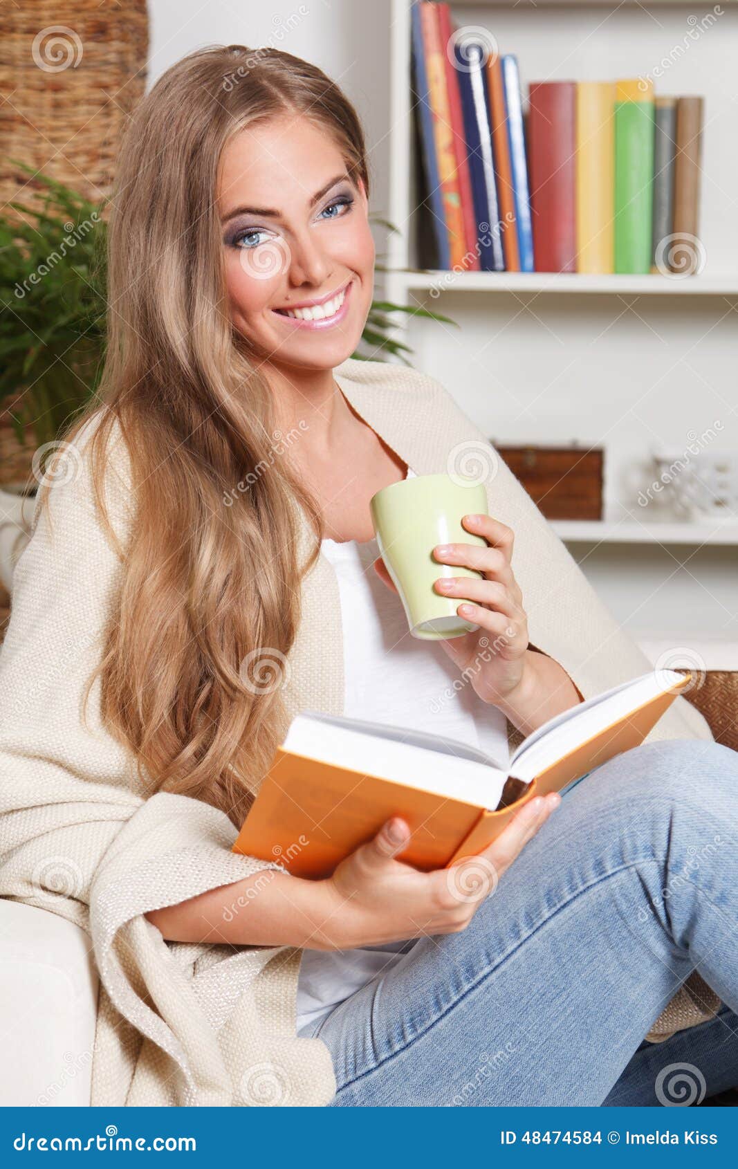 Chá bebendo da mulher feliz ao ler na sala de visitas