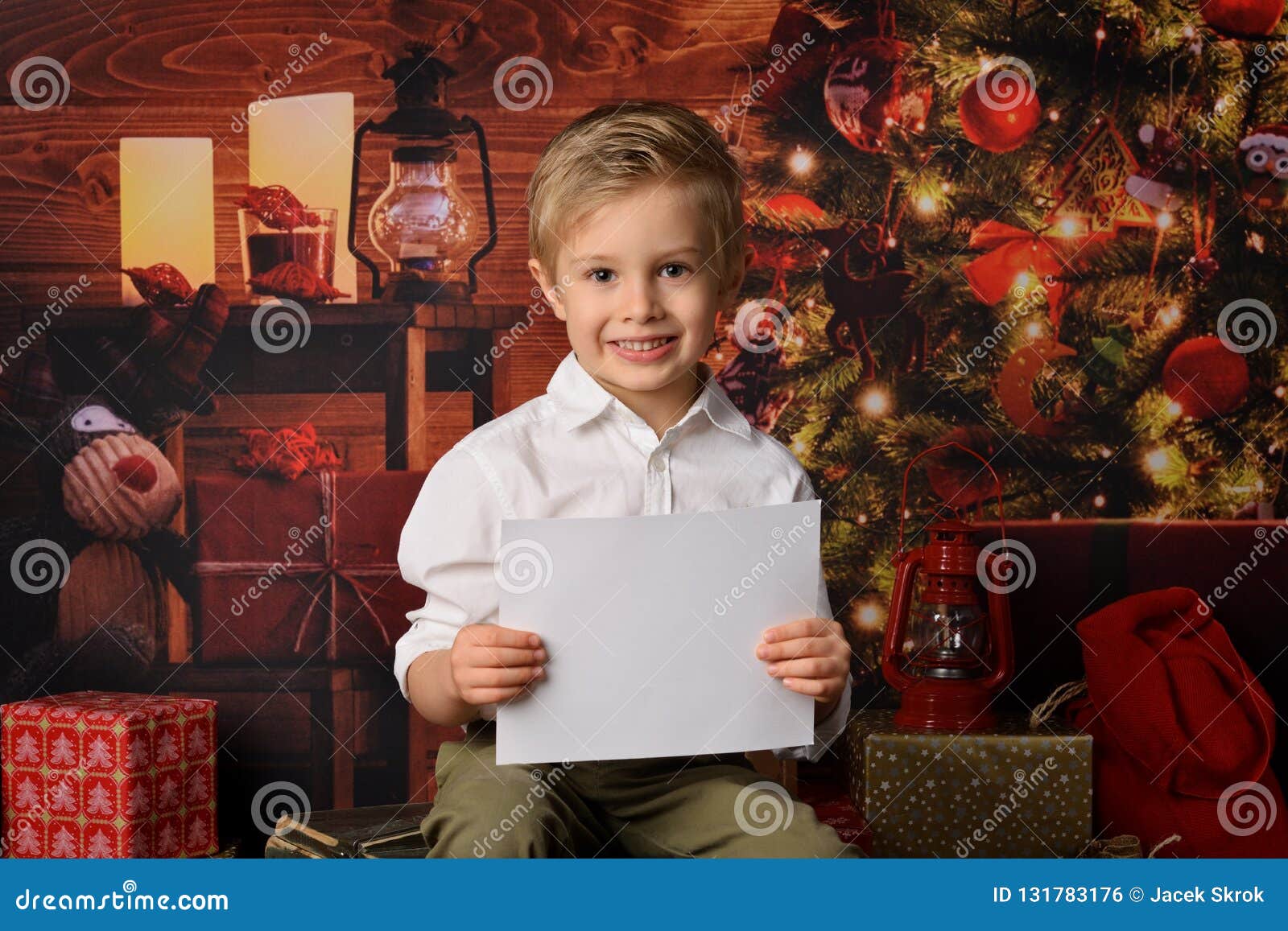 Chłopiec ubierająca w Święty Mikołaj bożych narodzeniach. Cztery lat chłopiec jest ubranym białego koszulowego mienia pustego prześcieradło biała księga na Bożenarodzeniowym tle
