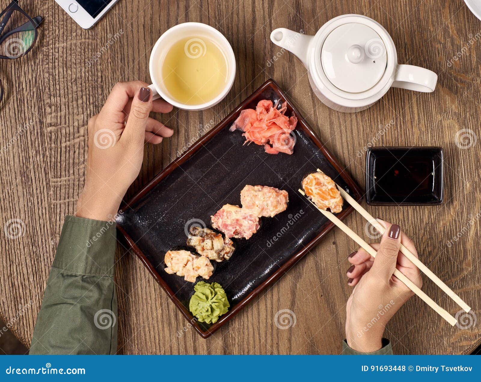 Cibo dei sushi con i bastoni di bambù. Flatlay Primo piano delle mani della donna con i bastoncini di bambù che mangiano i sushi con tè verde