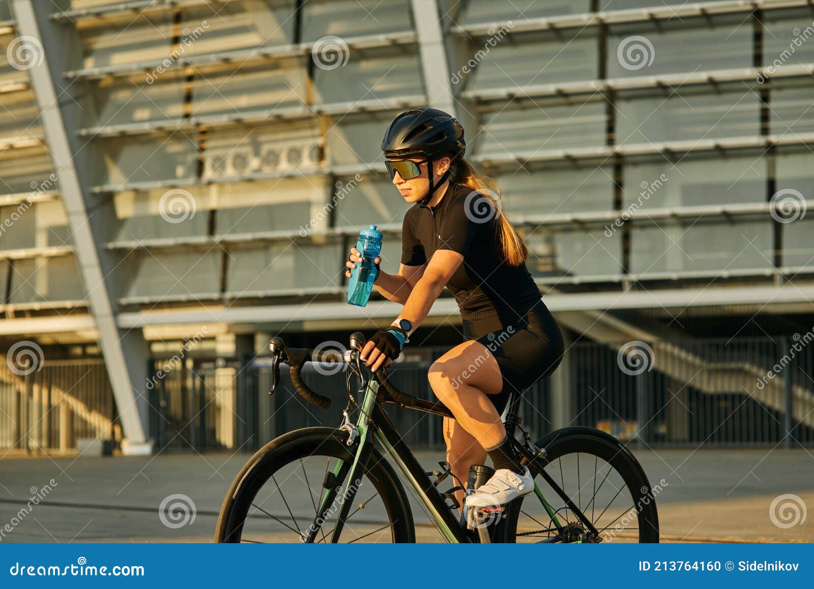 Ciclista Profesional Femenina En Ropa De Ciclismo Negro Y Equipo De Protección Sosteniendo Botella De Agua Mientras Monta En Bicic Foto archivo - Imagen de actividad, persona: 213764160