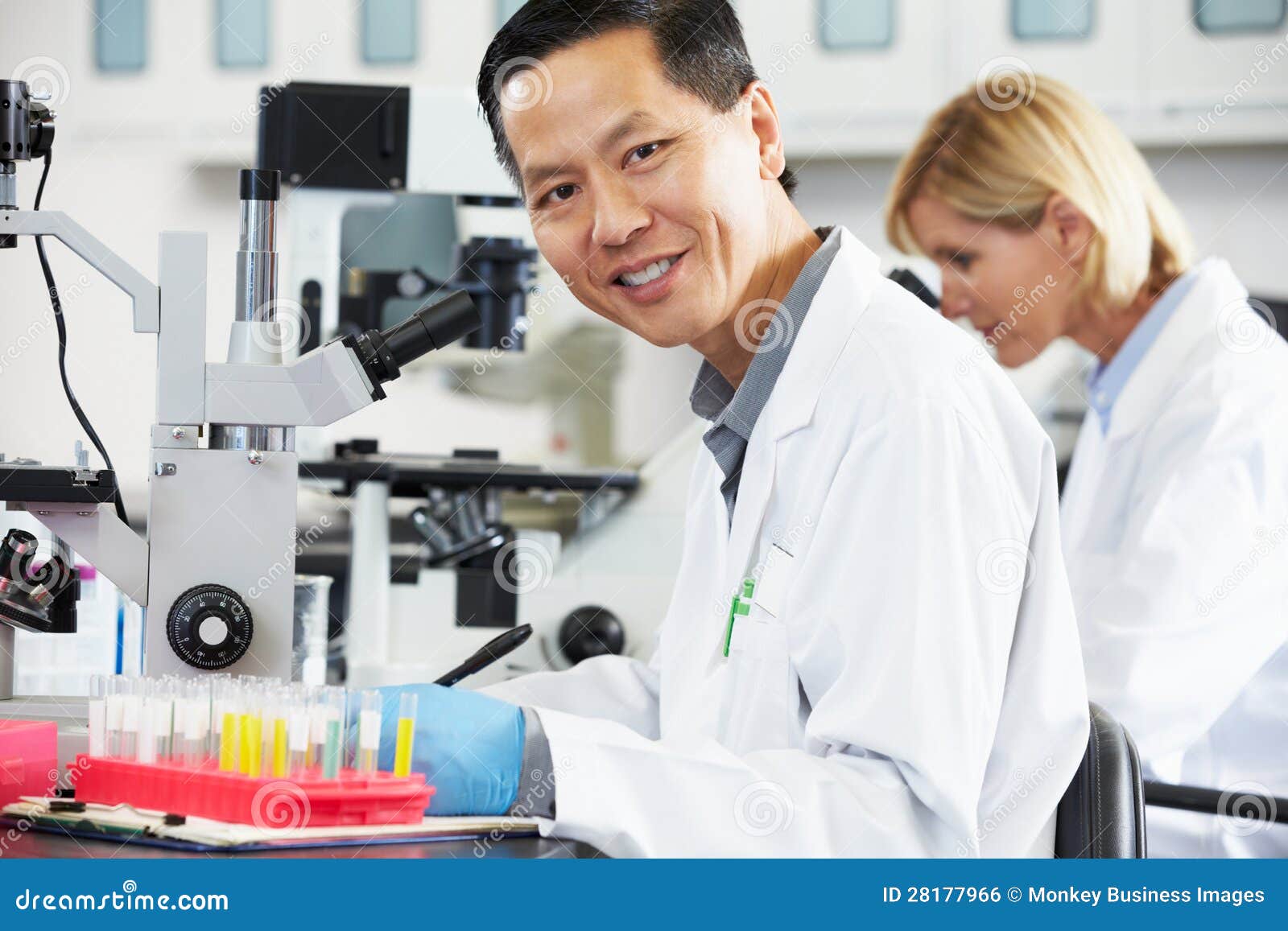 Científicos de sexo masculino y de sexo femenino que usan los microscopios en la sonrisa del laboratorio